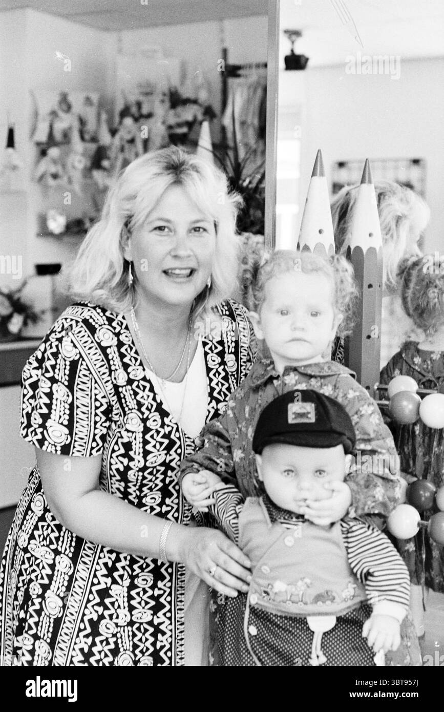 Kinderboutique Boefje Cronjéstraat Haarlem Generaal Cronjéstraat Niederlande, Whizgle News, Dutch Desk, Niederlande, 1950 - 2000 am 20-08-1997. Das Bild enthält diese Themen. In einem hellen Innenbereich steht eine Frau neben zwei Puppen. Sie hat schulterlange, wellige blonde Haare und trägt ein gemustertes Kleid mit schwarz-weißen Motiven, die einen lebhaften Kontrast zu ihrem fröhlichen Auftreten bilden. Ihr Ausdruck ist warm und einladend mit einem leichten Lächeln. Die Puppen, die eine vorne und die andere leicht hinten positioniert sind, sind deutlich gestylt. Die vordere Puppe hat lockiges Haar und Unkraut Stockfoto