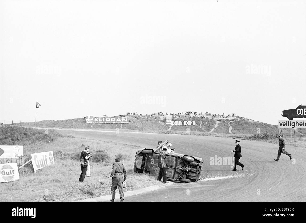 Formel-2-Rennen auf dem Zandvoort-Kurs. Zandvoort, Whizgle News, Dutch Desk, Niederlande, 1950 - 2000 am 05-06-1965. Diese Themen werden in der Abbildung angezeigt. In dieser Szene wird eine Landschaft von einer kurvenreichen Straße dominiert, die sich nach rechts biegt. Die Straße wird von grasbewachsenen Flächen begrenzt, die im Hintergrund leicht abschüssig sind, wo eine Reihe von Schildern deutlich zu sehen ist, die ein Gefühl von Lage und Kontext schaffen. Einige dieser Schilder, die teilweise verdeckt sind oder aus dem Blickwinkel verschwinden, deuten auf eine Verbindung zu Automobilthemen hin, was möglicherweise auf Sponsoring- oder Sicherheitsbotschaften hinweist. Auf dem Asphalt, ein sma Stockfoto