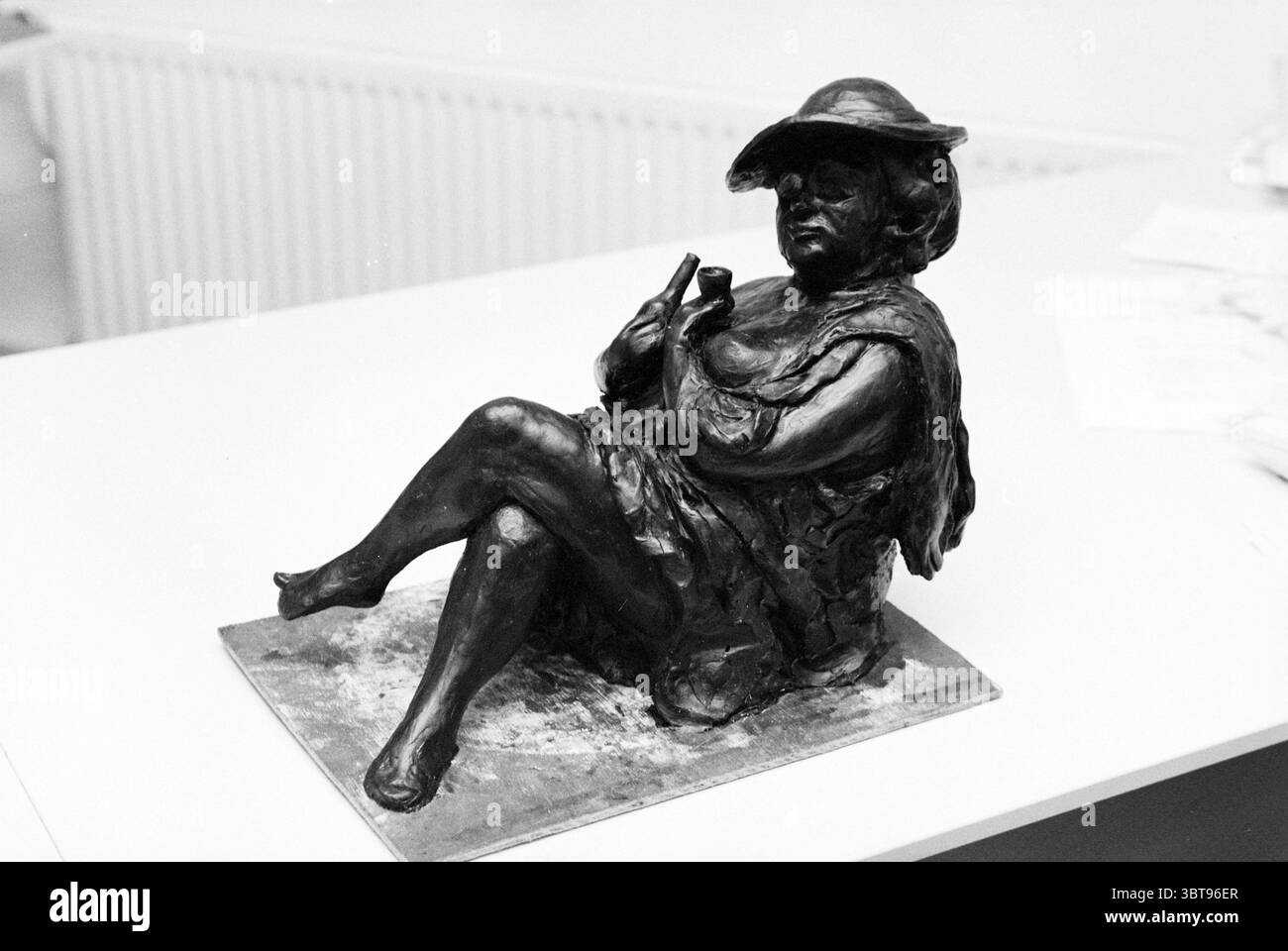 Statue Kerkplein Zandvoort Zandvoort Kerkplein, Whizgle News, Dutch Desk, Niederlande, 1950 - 2000 am 26-11-1997. Das Bild enthält diese Themen. Die Szene zeigt eine Bronzeskulptur einer sitzenden weiblichen Figur, die ein Gefühl entspannter Eleganz ausstrahlt. Die Frau ist mit einem leicht zur Seite geneigten Körper dargestellt, der auf dem linken Arm liegt, während ihr rechter Arm am Ellenbogen gebeugt ist und etwas zart hält. Sie trägt einen breitkrempigen Hut, der ihrem Aussehen einen Hauch von Raffinesse und Verspieltheit verleiht. Die Skulptur ist in einem satten, dunklen Metallic-Farbton dargestellt, der das helle U-Boot einfängt Stockfoto