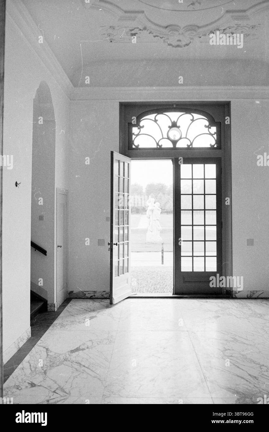 Blick mit Statue des Beeckestijn Anwesens Velsen-Zuid, Whizgle News, Dutch Desk, Niederlande, 1950 - 2000 am 15-05-1969. Diese Themen werden in der Abbildung angezeigt. Die Szene zeigt einen eleganten Innenraum, der sich durch seine Geräumigkeit und raffinierte architektonische Details auszeichnet. Das Licht kommt sanft durch eine Reihe von Doppeltüren ein, die mit komplizierten Designs verziert sind und einen Blick auf einen Außenbereich dahinter ermöglichen. Die Türen sind in einem gedämpften grünen Farbton lackiert und ergänzen die hellen Wände, die glatt sind. Der Boden besteht aus poliertem Marmor, der eine Mischung aus hell und dunkler zeigt Stockfoto