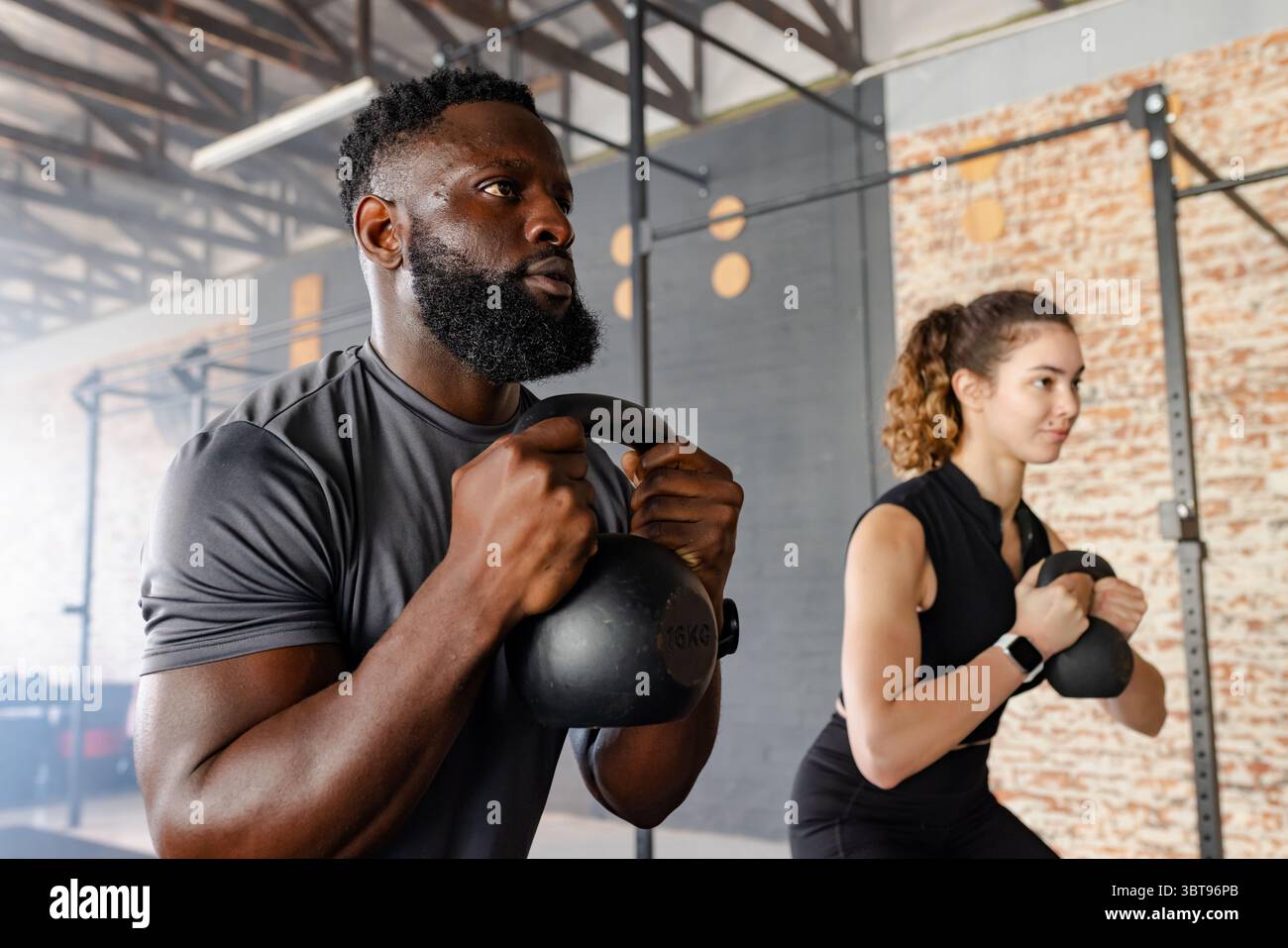 Verschiedene Workout-Partner führen Kettlebell-Kelch-Squats im Fitnessstudio mit Pull-Up-Rig durch Stockfoto