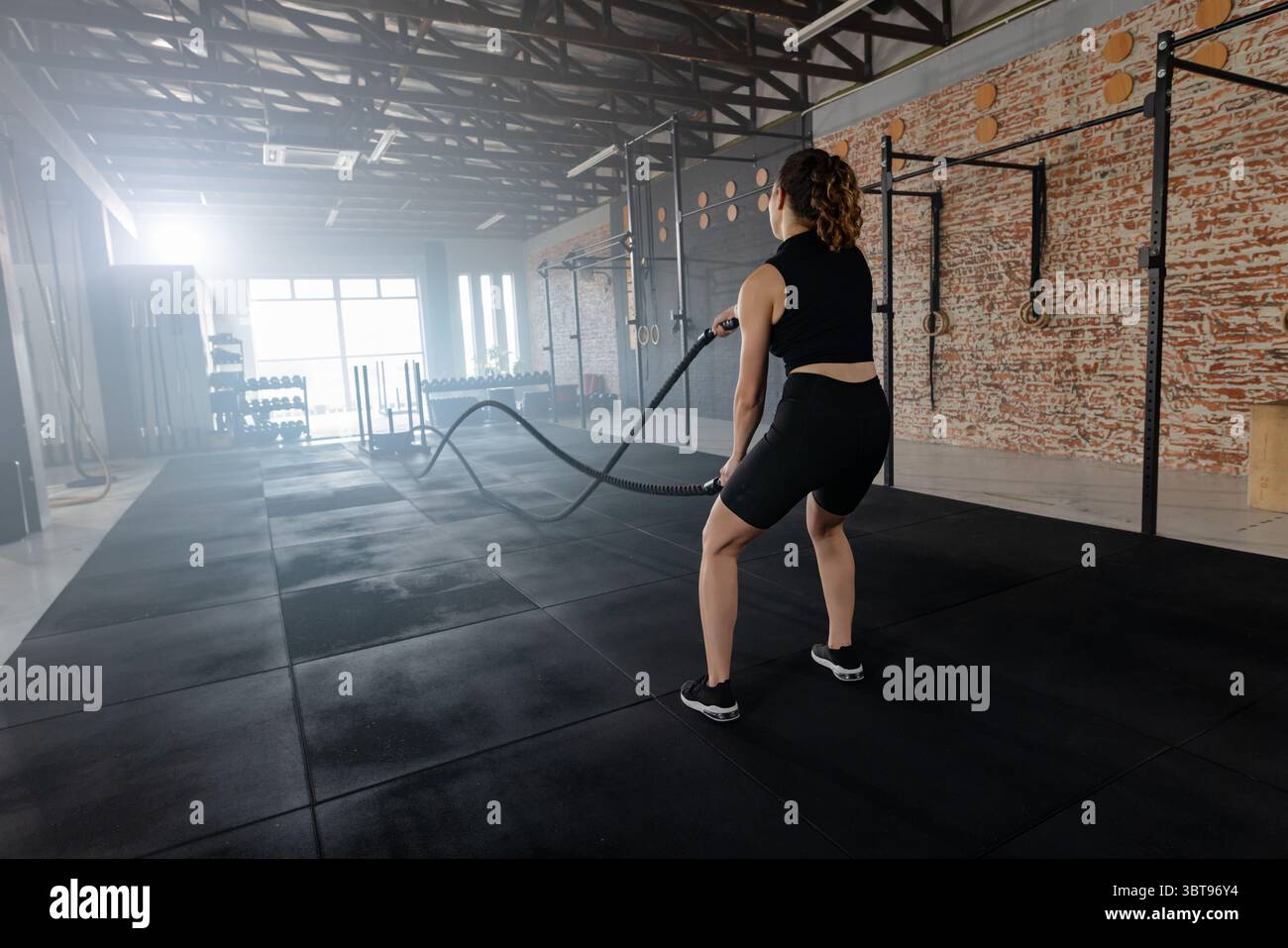Frau schwingt Kampfseile auf Matten im Fitnesscenter mit Kettlebells und Pull-up-Rig, Kopierraum Stockfoto