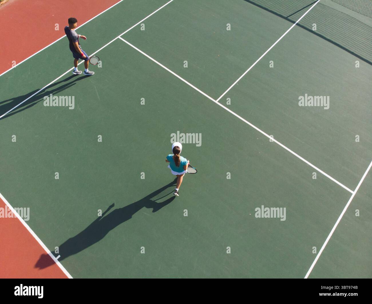 Verschiedene Gegner spielen Tennis mit Schlägern auf dem Hartplatz im Freien unter der Sonne und werfen lange Schatten Stockfoto