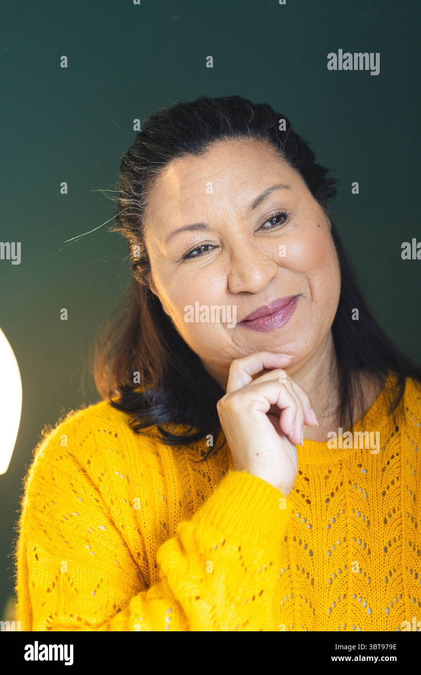 Frau mit gelbem Pullover, das Kinn auf der Hand liegend, während sie außerhalb der Kamera im privaten Zimmer mit Lampe blickte Stockfoto