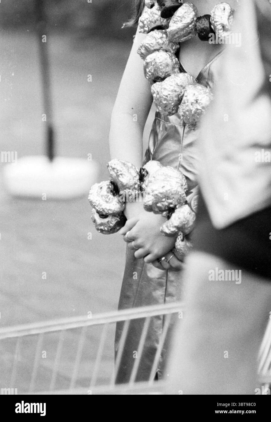 Supermarket CART Act, Whizgle News, Dutch Desk, Niederlande, 1950 - 2000 am 16-04-1993. Das Bild enthält diese Themen. Die Szene zeigt eine Person in einem glänzenden Outfit, das einen silbernen oder metallischen Farbton reflektiert und einen auffälligen und auffälligen Look verleiht. Der Stoff der Kleidung wirkt glatt und elegant drapiert und betont die Silhouette der Figur. Um die Arme der Person herum befinden sich mehrere große, glänzende Verzierungen, die an Felsen oder abstrakte Skulpturen aus einem ähnlichen metallischen Material erinnern und dem Gesamtlook einen skurrilen und avantgardistischen Touch verleihen. T Stockfoto