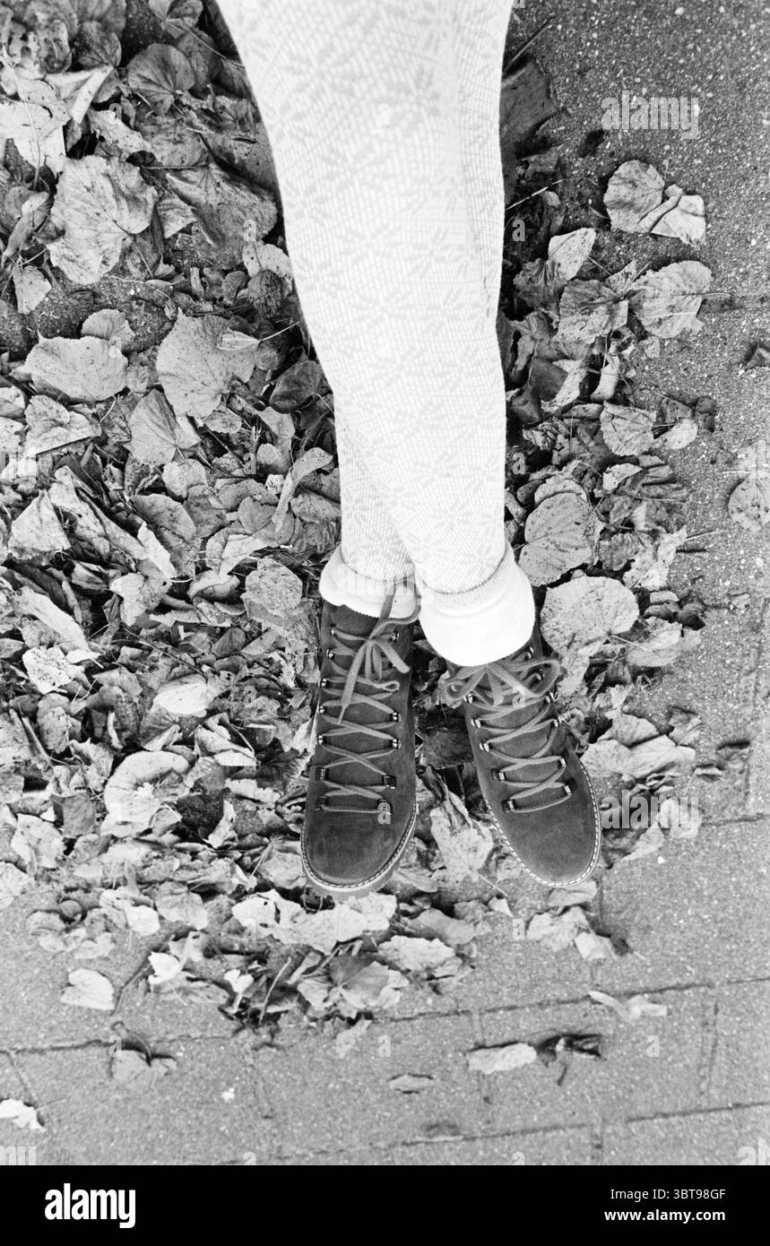 Fashion Fotos Kurier Fashion, Whizgle News, Dutch Desk, Niederlande, 1950 - 2000 am 19-09-1982. Diese Themen werden in der Abbildung angezeigt. Im Vordergrund der Szene liegt ein Paar braune Schnürschuhe vor dem Hintergrund frischer, trockener Blätter, die über den Boden verstreut sind. Die Schuhe sind getragen, aber stilvoll und bieten eine Mischung aus Robustheit und Komfort, die sich nahtlos in die natürliche Umgebung einfügen. Die Beine, die mit hellen, gemusterten Leggings bedeckt sind, sind lässig positioniert, erstrecken sich nach außen und bilden den Rahmen für die Schuhe. Die Leggings haben ein dezentes Design, das der visuellen Komposition Textur verleiht. S Stockfoto