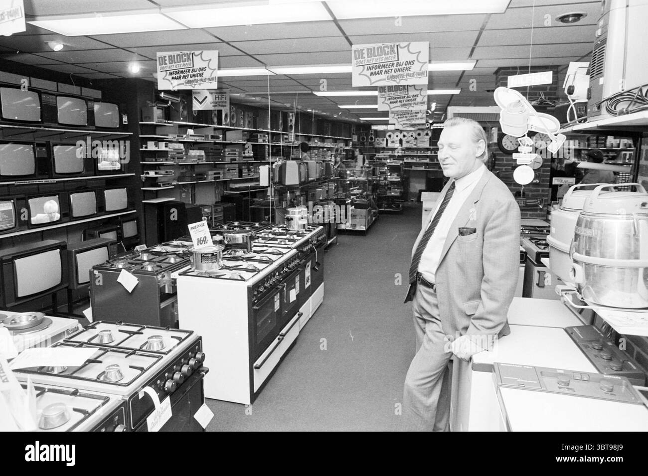 Mr. De Block Radio und TV Fall Hillegom. Personen Unternehmen Hillegom, Whizgle News, Dutch Desk, Niederlande, 1950 - 2000 am 26-01-1982. Das Bild enthält diese Themen. Die Szene spielt in einem belebten Elektronik- und Gerätegeschäft, das einen Vintage-Charme ausstrahlt. Reihen verschiedener Küchengeräte und Elektronik erzeugen eine lineare Perspektive, die den Blick nach hinten zieht. Auf der linken Seite sind mehrere große Fernsehgeräte deutlich sichtbar auf den Ständen zu sehen, deren Bildschirme dunkel sind, und einige Sets zeigen einen Hauch von Statik. Die Fernseher sind in eleganten schwarzen Rahmen verpackt, Emphas Stockfoto