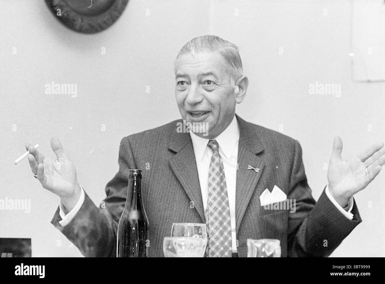 Porträt-Burg. Nielen Heemskerk Mayors Heemskerk Municipal Council, Whizgle News, Dutch Desk, Niederlande, 1950 - 2000 am 08.12.1970. Das Bild enthält diese Themen. Die Szene fängt einen Mann in einem gut zugeschnittenen Anzug ein, der ein lebhaftes und animiertes Verhalten ausstrahlt. Er sitzt an einem Tisch und zeigt mit beiden Händen Gesten, dass er mitten im Gespräch ist. Sein Ausdruck ist animiert, zeigt ein verspieltes Lächeln und ein einnehmendes Verhalten, was darauf hindeutet, dass er wahrscheinlich eine humorvolle Anekdote oder eine fesselnde Geschichte teilt. Der Anzug ist dunkel mit dünnen Streifen, ergänzt durch ein helles Hemd und ein Stockfoto