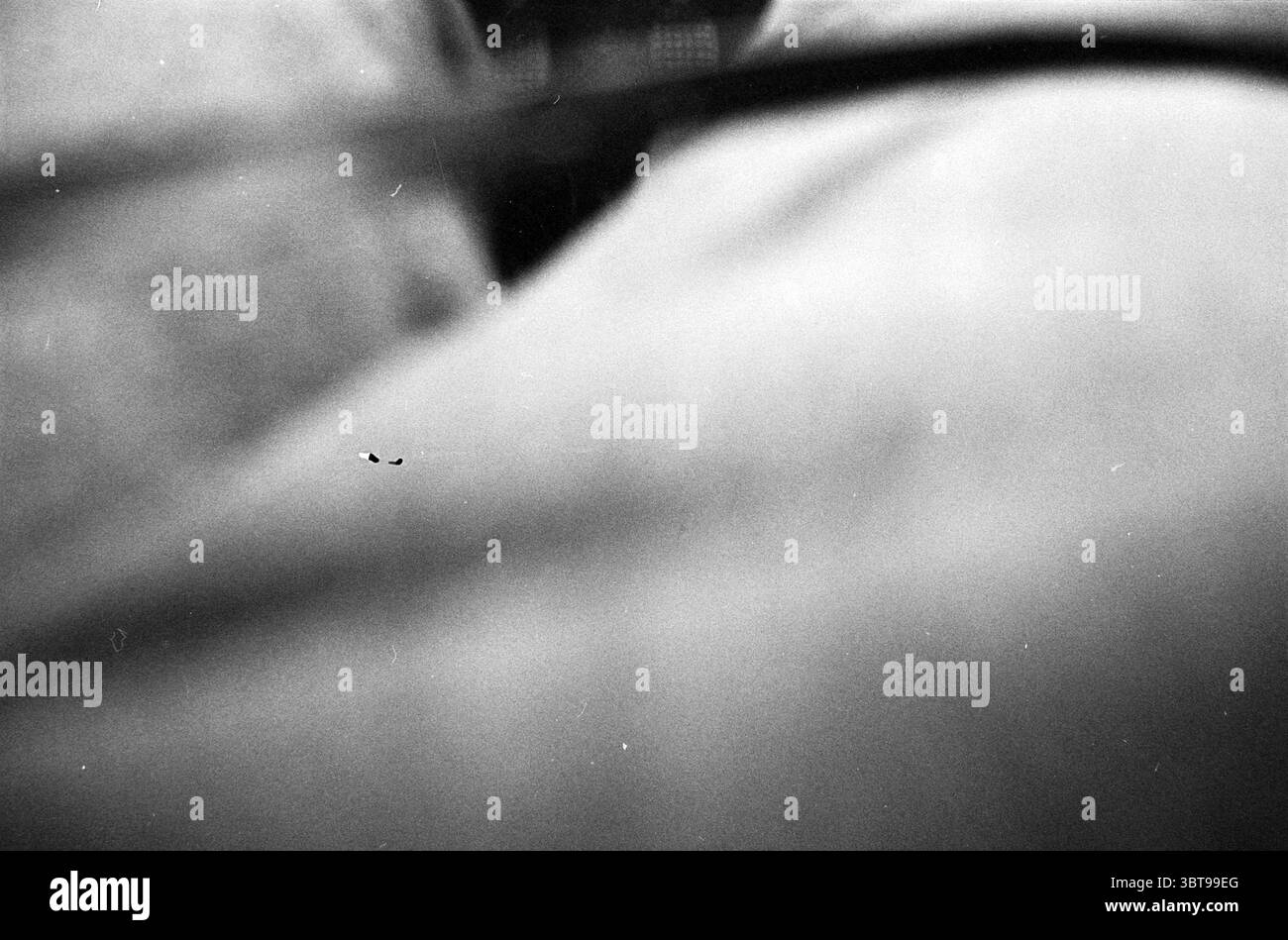 Wiederverwendbar., Whizgle News, Dutch Desk, Niederlande, 1950 - 2000. Das Bild enthält diese Themen. Die Szene bietet eine Nahansicht, die Textur und Form betont, hauptsächlich in Grautönen. Der Vordergrund zeigt weiche, unscharfe Kurven, die auf die Konturen von Stoff oder Haut hinweisen und sich zu einem leicht körnigen Hintergrund verschmelzen. Die Beleuchtung ist stummgeschaltet und erzeugt sanfte Schatten, die ein Gefühl von Tiefe erzeugen und gleichzeitig eine monochromatische Farbpalette beibehalten. Es gibt ein subtiles Zusammenspiel von hellen und dunklen Bereichen, das die Aufmerksamkeit auf die weichen Konturen und Falten lenkt und die haptische Qualität des M verbessert Stockfoto