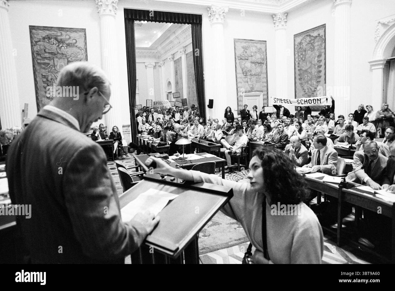 Anhörung zu Plänen Spiegelpolder und Spiegelplas in Provinciehuis Haarlem Niederlande, Whizgle News, Dutch Desk, Niederlande, 1950 - 2000 am 08.09.1992. Das Bild enthält diese Themen. Die Szene entfaltet sich in einer großen, historischen Kammer, die von hohen Decken und eleganten architektonischen Details wie verzierten Zierleisten und großen Fenstern geprägt ist, die ein weiches, diffuses Licht den Raum ausfüllen lassen. Die Wände sind mit aufwendig geschnitzten Paneelen verziert, die ein Gefühl von Raffinesse verleihen. Im Vordergrund steht ein Sprecher an einem Rednerpult, der einem großen Publikum gegenüber steht. Die Person trägt f Stockfoto