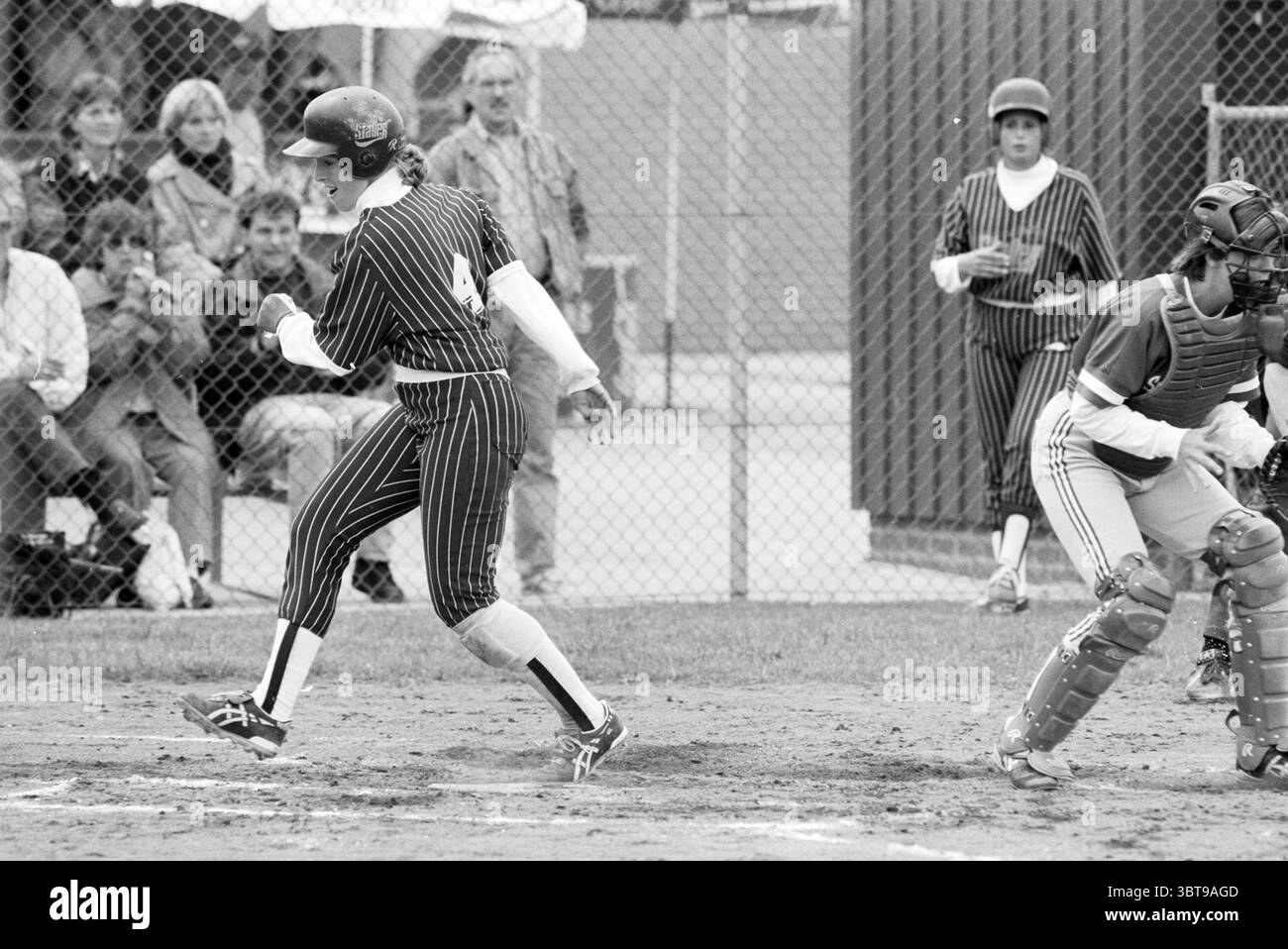 Softball Terrasvogels - Sparks, Whizgle News, Dutch Desk, Niederlande, 1950 - 2000 am 18-06-1993. Diese Themen werden in der Abbildung angezeigt. In der Szene entfaltet sich ein dynamischer Moment auf einem Baseballfeld. Ein Spieler in einer gestreiften schwarz-weißen Uniform stürzt auf die Heimplatte, sein Körper ist entschlossen nach vorne geneigt. Die Uniform hat eine markante Zahl auf der Rückseite, und die Kappe ist nach unten gezogen, wodurch ihr Gesicht teilweise verdeckt wird. Ihre Stollen werfen beim Sprinten eine kleine Staubwolke aus dem Innenfeld auf. Auf der rechten Seite ist ein Fänger in Schutzkleidung und Helm vorbereitet und fokussiert. Seine Pos. Stockfoto