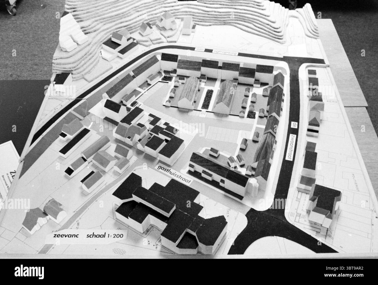 Modell Wijk aan Zee das Gebiet zwischen Gasthuisstraat de Zwaanstraat Van Ogtropweg mit Zeevanc Pflegeheim, Whizgle News, Dutch Desk, Niederlande, 1950 - 2000 am 23-11-1983. Das Bild enthält diese Themen. Die Szene zeigt ein Architekturmodell auf einer flachen Fläche, das ein detailliertes Layout einer kleinen Stadt oder Gemeinde zeigt. Das Modell besteht aus verschiedenen Gebäuden, Straßen und Grünflächen, die in einer monochromatischen Palette von Schwarz, weiß und Grautönen dargestellt sind, was ihm eine schlanke, moderne Ästhetik verleiht. Gebäude variieren in Höhe und Form, einige mit Flachdächern und andere mit spor Stockfoto