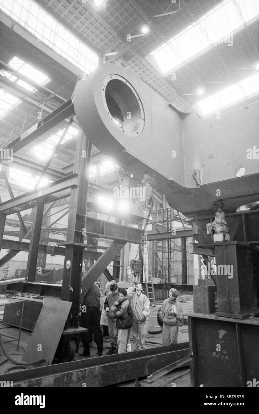 Open Day Figee Cranes, Whizgle News, Dutch Desk, Niederlande, 1950 - 2000 am 06-02-1992. Das Bild enthält diese Themen. In einem großen industriellen Umfeld zeichnet sich die Szene durch eine geräumige, hohe Umgebung aus, die mit schweren Maschinen und Metallkonstruktionen gefüllt ist. Die Architektur verfügt über freiliegende Strahlen und ein gitterähnliches Muster aus Oberlichtern, wodurch weiches, diffuses natürliches Licht durchfiltert wird und eine Mischung aus Schatten und beleuchteten Flecken auf dem Boden entsteht. In der Mitte dominiert eine erhebliche Metallstruktur, die möglicherweise Teil von Maschinen oder Geräten ist, den Vordergrund, seine Oberfläche Stockfoto