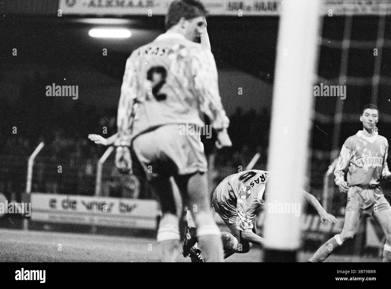 Telstar - Volendam, Whizgle News, Dutch Desk, Niederlande, 1950 - 2000 am 09-11-1993. Diese Themen sind in der Abbildung dargestellt. In der Szene werden mehrere Spieler inmitten eines angespannten Fußballspiels gefangen, wodurch eine Atmosphäre entsteht, die voller Energie und Dringlichkeit ist. Die Umgebung ist ein Stadion im Freien unter der Decke der Nacht. Der Hintergrund ist schwach beleuchtet, überwiegend mit tiefen Schatten, die mit hellen Flutlichtern, die Teile des Spielfeldes beleuchten, kontrastiert werden. Die gesamte Farbpalette neigt sich monochrom mit Schwarz-, weiß- und Grautönen an und unterstreicht die dramatische Stimmung. Im Stockfoto