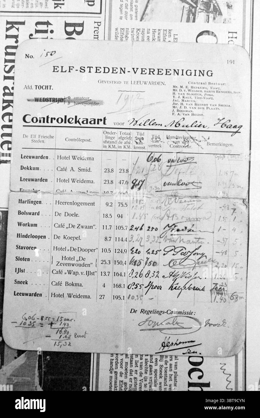 Elfstedentocht Karte von 1912 von PIM Mulier Skating, Whizgle News, Dutch Desk, Niederlande, 1950 - 2000 am 17-01-1985. Das Bild enthält diese Themen. Die Szene zeigt eine Sammlung von Dokumenten mit einem Vintage-Look, überwiegend in monochromen Tönen, die ihr ein Gefühl von Nostalgie verleihen. Die Papiere sind mehrschichtig, überlappend, wodurch ein strukturierter Look entsteht. Im Vordergrund befindet sich eine Steuerkarte, die als Herzstück auffällt. Die Oberfläche ist leicht zerknittert und weist Alterserscheinungen auf, mit handgeschriebenen Einträgen und einer Kombination verschiedener Tintenfarben, überwiegend schwarz und blau Stockfoto