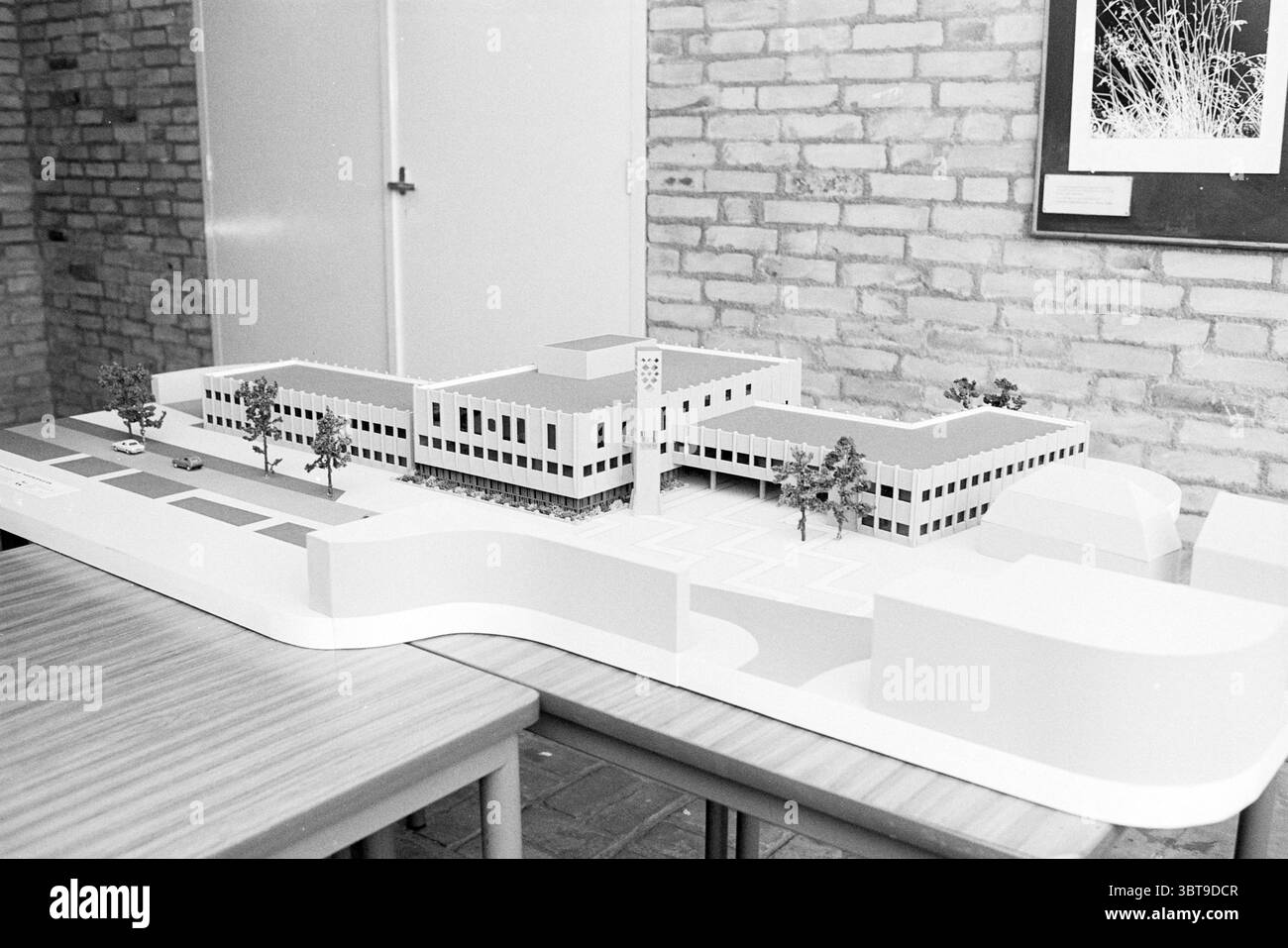 Modell des neuen Rathauses Heemskerk Municipal Council of Heemskerk Model, Whizgle News, Dutch Desk, Niederlande, 1950 - 2000 am 07-11-1977. Dies sind die Themen im Bild. Die Szene zeigt ein detailliertes Architekturmodell eines Gebäudes, das in monochromen Tönen dargestellt wird. Das Gebäude ist auf einer Ebenen Fläche angeordnet und weist ein rechteckiges Layout mit zwei separaten Abschnitten auf, die durch einen zentralen Innenhof miteinander verbunden sind. Um das Modell herum sind sorgfältig gefertigte Miniaturbäume angebracht, die einen Hauch von Grün hinzufügen und eine landschaftlich gestaltete Umgebung vorschlagen. Die Fassade des Gebäudes ist sauber und minimalistisch, charakterisiert B Stockfoto