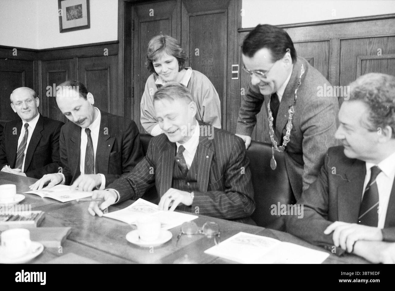 Präsentation des Heftes über 125 Jahre Halfweg Zuckerfabrik Übergabe und Transfers Halfweg Haarlemmerstraatweg, Whizgle News, Dutch Desk, Niederlande, 1950 - 2000 am 26.04.1988. Dies sind die Elemente im Bild. Die Szene zeigt eine formelle Zusammenkunft in einem gut beleuchteten Innenraum, der durch Holztäfelungen gekennzeichnet ist, die dem Ambiente ein Gefühl von Wärme und Autorität verleihen. Ein langer Tisch aus dunklem Holz dominiert den Vordergrund, um den sechs Personen sitzen, die jeweils in formeller Kleidung gekleidet sind, die eine wichtige Versammlung oder Unterzeichnungszeremonie nahelegt. Die zentrale Figur, sitzend Stockfoto