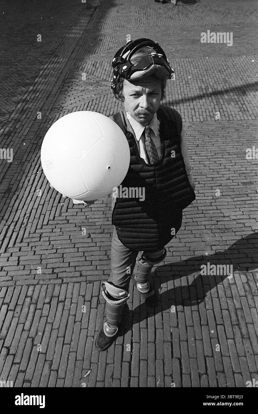 Louis Ferron mit Ballpersonen, Whizgle News, Dutch Desk, Niederlande, 1950 - 2000 am 13.09.1968. Diese Themen werden in der Abbildung angezeigt. Die Szene zeigt eine einzigartige Figur, die auf einer strukturierten Backsteinoberfläche steht, wahrscheinlich auf einem Bürgersteig oder einem Außenbereich. Die Person trägt ein spezielles Outfit, bestehend aus einem maßgeschneiderten Anzug und einem ungewöhnlichen Schutzausrüstung-Set, das eine gepolsterte Weste und dicke Knieschoner umfasst, was eine Mischung aus formeller und sportlicher Ästhetik suggeriert. Ihr Kopf ist mit einem helmähnlichen Accessoire verziert, das der Szene ein verspieltes oder absurdes Element verleiht. Der Ausdruck des Einzelnen ist ernst, W Stockfoto