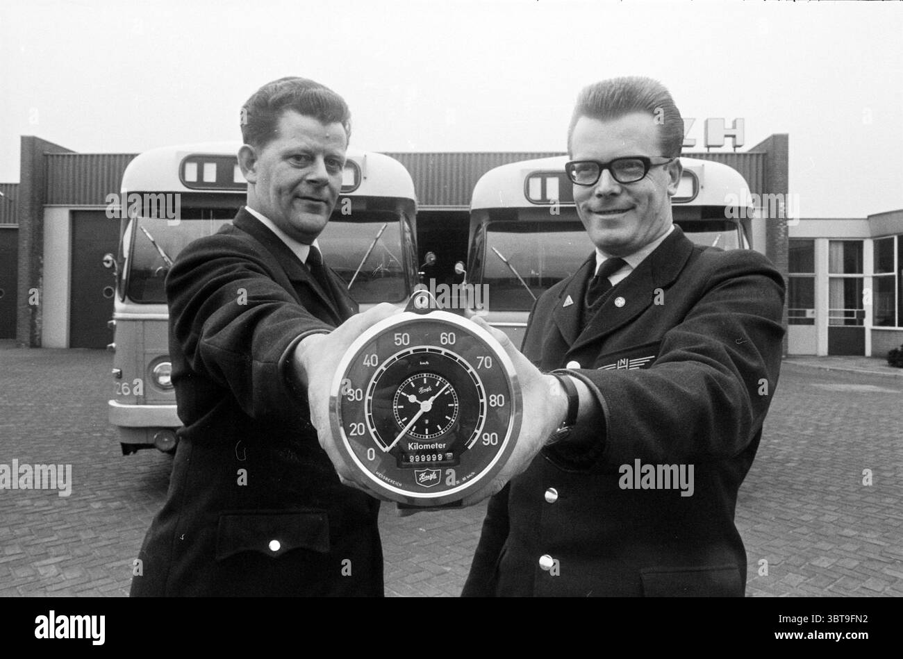 Zwei Busfahrer mit einem Fahrtenschreiber, der 999999,9 km registriert hat, Whizgle News, Dutch Desk, Niederlande, 1950 - 2000. Diese Themen sind in der Abbildung dargestellt. Die Szene zeigt zwei Männer, die im Vordergrund stehen, jeder in formellen, dunklen Uniformen gekleidet, die ein Gefühl von Professionalität und Autorität vermitteln. Sie haben unterschiedliche Frisuren – eine hat einen klassischen, ordentlich gestylten Look, während die andere eine flachere Frisur mit einer leichten Welle zeigt. Beide blicken mit selbstbewusstem Ausdruck zur Kamera, was auf Stolz auf ihre Rollen hindeutet. In ihren Händen halten sie eine große analoge Stoppuhr, die ich Stockfoto