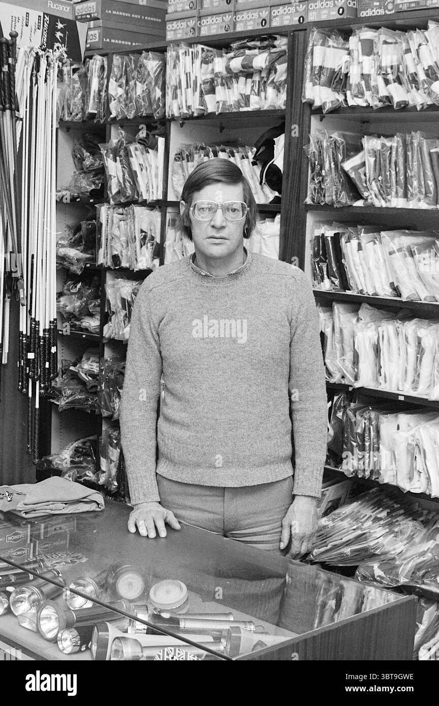 Adri Zwaanswijk : Niederländisch. Korfballtrainer A'Damm. Korfball People Sports, Whizgle News, Dutch Desk, Niederlande, 1950 - 2000 am 11-03-1976. Dies sind die Themen im Bild. Die Szene zeigt einen älteren Mann, der selbstbewusst hinter einer Glasplatte steht. Er trägt einen hellgrauen Pullover und hat eine Brille auf der Nase, die ihm ein nachdenkliches Aussehen verleiht. Sein Haar ist kurz und ordentlich gekämmt, und er trägt ein freundliches, aber professionelles Verhalten. Um ihn herum sind die Wände mit einer Reihe von Waren gesäumt, in denen verschiedene Artikel nach Art organisiert sind. Die Regale sind gefüllt Stockfoto