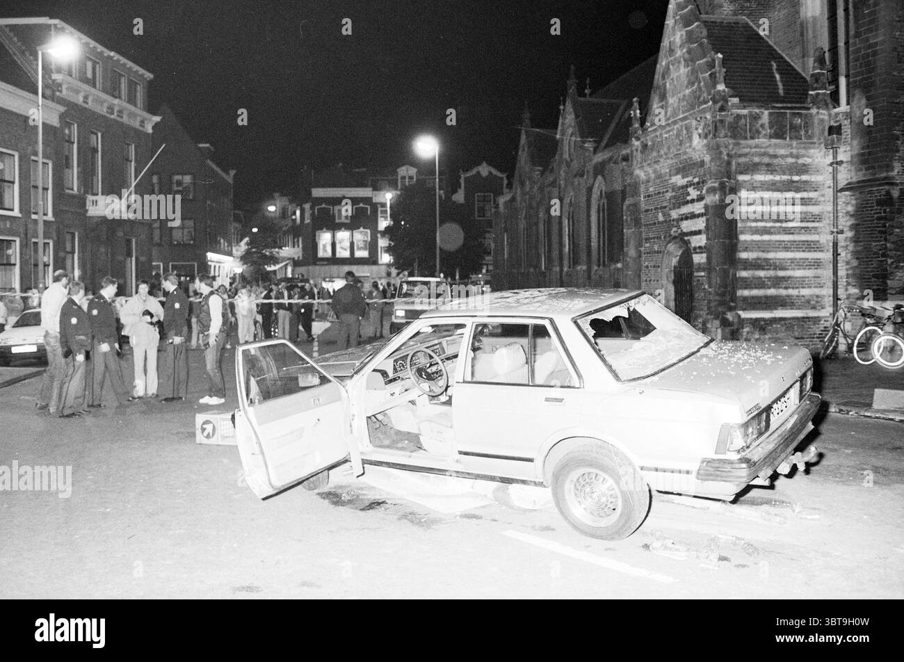 River Fish Market Schießen Unfälle Unfälle Unfälle Schießen Polizei Haarlem Riviervismarkt Niederlande, Whizgle News, Dutch Desk, Niederlande, 1950 - 2000 am 12-06-1987. Das Bild enthält diese Themen. Die Szene spielt nachts, beleuchtet von Straßenlaternen, die ein raues Licht über die Umgebung werfen. Im Vordergrund befindet sich ein beschädigtes Auto mit offener Tür, das Innere ist sichtbar und Objekte sind verstreut. Das Fahrzeug wirkt alt, hat ein leicht abgenutztes Design und es gibt sichtbare Anzeichen von Vandalismus oder vorherigen Störungen, wie z. B. zersplitterte Fenster. Im Hintergrund eine Gruppe von Leuten Stockfoto