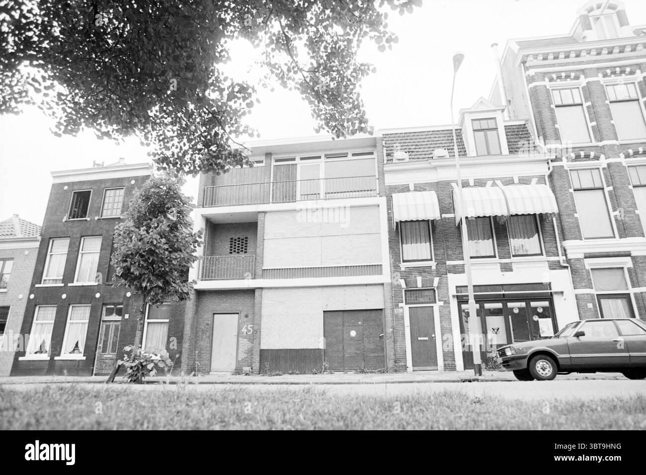 Erw. Hells Angels Place parklaan Haarlem Hells Angels Haarlem Parklaan Niederlande, Whizgle News, Dutch Desk, Niederlande, 1950 - 2000 am 25-07-1989. Das Bild enthält diese Themen. Die Szene präsentiert eine ruhige urbane Landschaft, die von gedämpften Tönen und einem Gefühl der Stille geprägt ist. Zwei Gebäude sind gut sichtbar dargestellt, jedes mit unterschiedlichen architektonischen Merkmalen. Auf der linken Seite zeigt ein schmales Gebäude aus rotem Backstein traditionelle Fensterrahmen mit aufwändigen Zierleisten über den Fenstern. Das Erdgeschoss hat große, verdunkelte Fenster, was wahrscheinlich auf mangelnde Aktivität oder ein leeres Spa hinweist Stockfoto