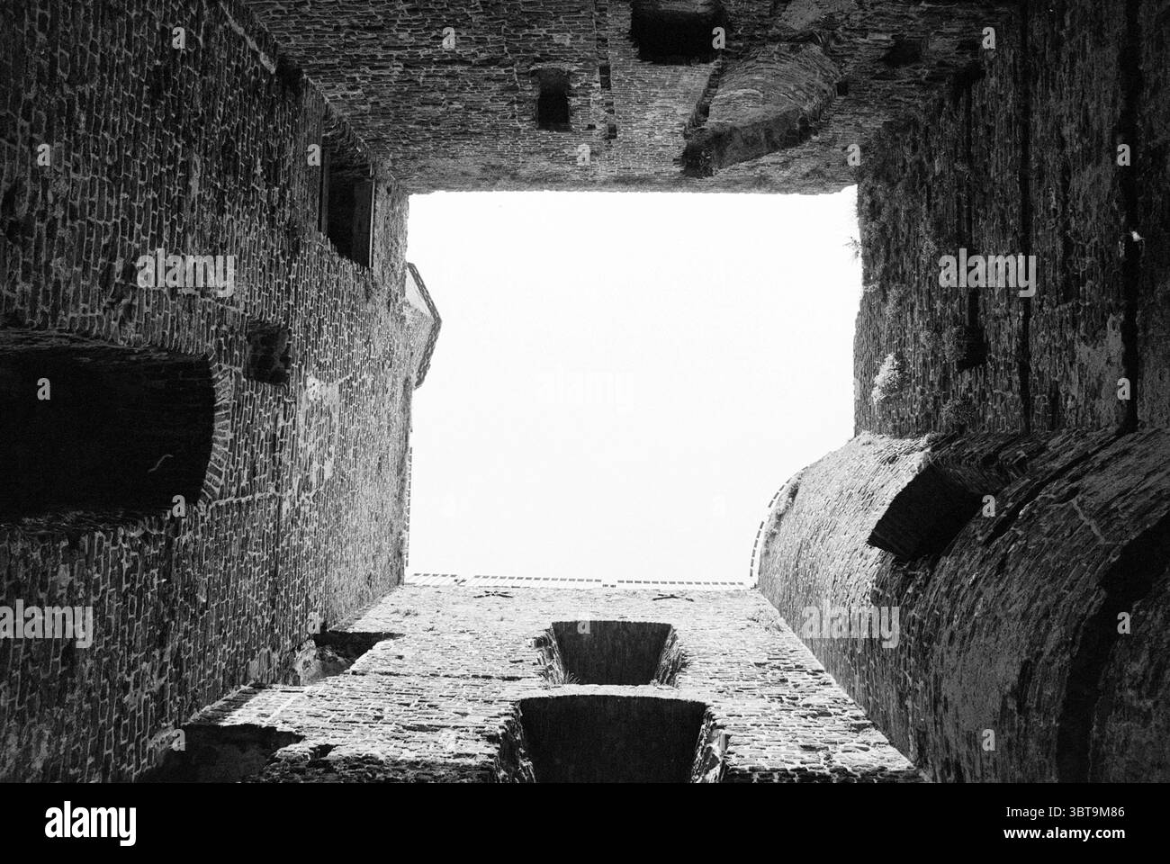 Hauptturm Brederode Ruine Ruin Santpoort, Whizgle News, Dutch Desk, Niederlande, 1950 - 2000 am 06-07-1989. Das Bild enthält diese Themen. Die Szene fängt das Innere eines alten Steinbaus ein, mit Wänden, die hoch über ihnen ragen, und schafft eine vertikale visuelle Flucht in den Himmel. Die rauen, verwitterten Steine dominieren die Umgebung, die in Grautönen getönt sind, die auf Alter und Geschichte hinweisen, mit Flecken aus dunklerem Moos und helleren Steinen. Wenn man nach oben blickt, ist ein schmaler Streifen von hellem Licht zu sehen, der auf einen bewölkten Himmel hindeutet, während die Wände fast aufragend erscheinen und das Monum betonen Stockfoto