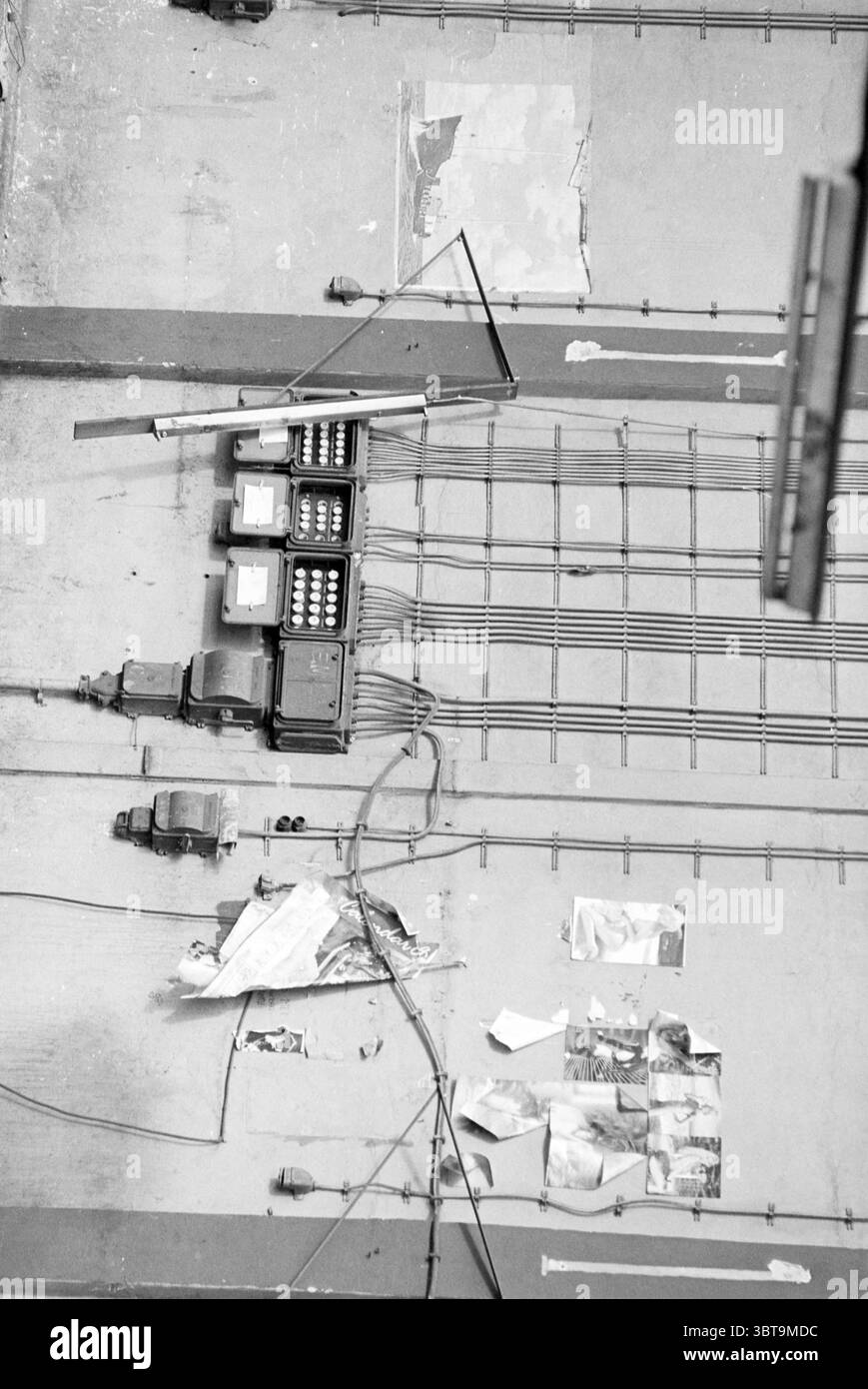 Abriss von Spaans Babcock, Whizgle News, Dutch Desk, Niederlande, 1950 - 2000 am 09-03-1993. Die Abbildung zeigt diese Themen. Die Szene zeigt eine Wand, die hauptsächlich aus einem gedämpften Grauton besteht, was ihr ein starkes, industrielles Feeling verleiht. Verschiedene Flecken der abblätternden Farbe deuten auf Alter und Verschleiß hin, während einige Bereiche dunklere Flecken aufweisen, die das strukturierte Aussehen noch verstärken. Auf der linken Seite schlängelt sich eine Reihe von Drähten über die Oberfläche, die zu mehreren schwarzen Schaltkästen zusammenlaufen, die an der Wand montiert sind. Diese Kästen sind leicht glänzend auf dem matten Hintergrund und ziehen das Auge mit ihrer geometrischen Form Stockfoto