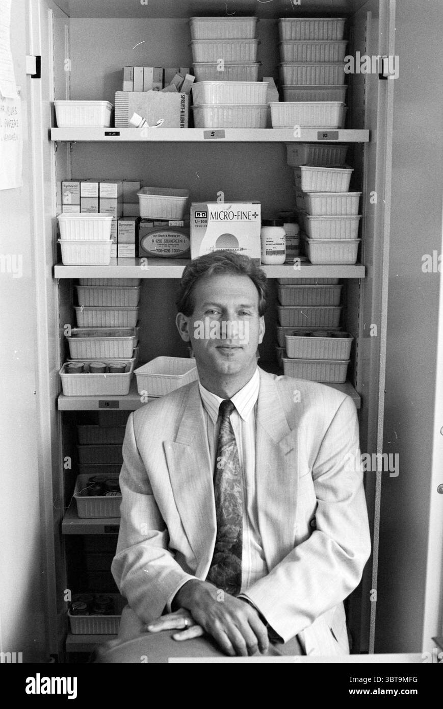 Direktor van Ruth Brijdersstichting, Whizgle News, Dutch Desk, Niederlande, 1950 - 2000 am 07-09-1993. Diese Themen sind in der Abbildung dargestellt. Die Szene zeigt einen Mann, der vor einem ordentlich organisierten Regal sitzt, gefüllt mit verschiedenen Behältern. Er trägt einen hellen, maßgeschneiderten Anzug mit dezenten Nadelstreifen, was ihm ein professionelles Aussehen verleiht. Der Anzug wird durch eine Krawatte mit gedämpftem Muster ergänzt, die einen Hauch von Persönlichkeit verleiht, ohne den Gesamtlook zu überfordern. Der Hintergrund zeigt eine Reihe flacher, weißer Behälter, die methodisch angeordnet und mit einer Reihe von gefüllt sind Stockfoto