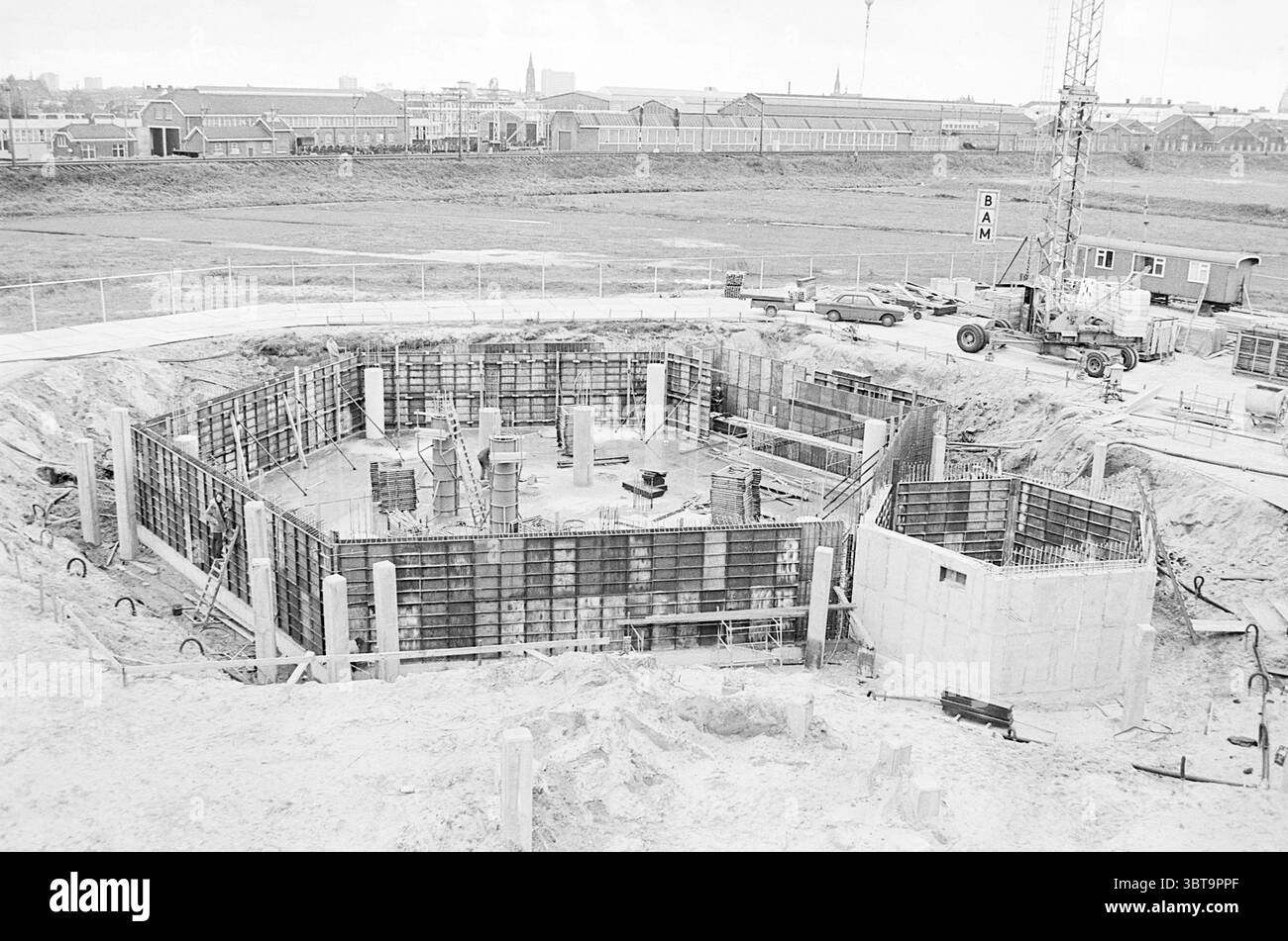 Baubüro H.D. + Bau der neuen Presse H.D. Haarlems Dagblad etc. Und IJmuider Courant and Koeri, Whizgle News, Dutch Desk, Niederlande, 1950 - 2000 am 25-10-1974. Diese Themen werden in der Abbildung angezeigt. Die visuelle Szene zeigt eine weitläufige Baustelle, die durch eine große, tiefe Ausgrabung gekennzeichnet ist, die ein Fundament in Bearbeitung zeigt. Das Gelände wird von einer Reihe vertikaler, armierter Betonformen eingerahmt, die ein rechteckiges Muster am Boden der Grube bilden. Diese Strukturen werden mit horizontalen Stützen gehalten, was auf einen methodischen Ansatz beim Bau hinweist. Surrou Stockfoto