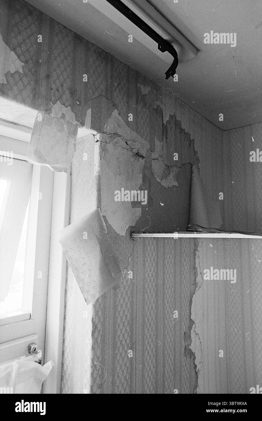 Undichte Rohre Heemskerk Legepipes, Whizgle News, Dutch Desk, Niederlande, 1950 - 2000 am 07-05-1973. Diese Themen sind in der Abbildung dargestellt. Die Szene zeigt eine Ecke eines Raumes, die sich durch ihren altertümlichen und sich verschlechternden Zustand auszeichnet. Die Wände tragen Überreste von abblätternder Tapete, die darunter Schichten freilegen, die ein noch lebendigeres Dekorationsschema andeuten. Die Farben, vorwiegend dezente Grau- und Weißtöne, wecken ein Gefühl der Vernachlässigung und veralteten Atmosphäre. Im linken Bereich des Rahmens lässt ein Fenster lichtes natürliches Licht eindringen, wodurch ein starker Kontrast zwischen den beleuchteten Bereichen und t entsteht Stockfoto
