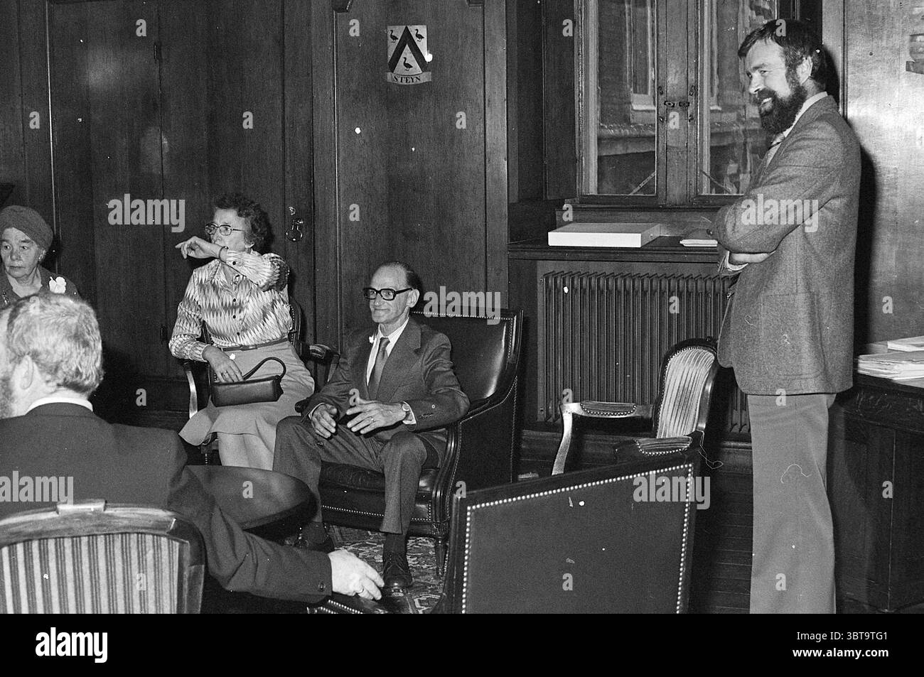 Kleine Gruppe versammelte sich in einem Empfangsraum. Whizgle News, Dutch Desk, Niederlande, 1950 - 2000. Die Abbildung zeigt diese Themen. Die Szene spielt in einem warm dekorierten Raum mit üppiger Holztäfelung, die ein Gefühl von Tradition und Formalität weckt. Die Beleuchtung ist weich und gedämpft, wahrscheinlich von Lampen, die strategisch platziert sind, um bestimmte Bereiche hervorzuheben, und verleiht dem Treffen eine gemütliche und doch ernste Atmosphäre. Im Vordergrund steht eine Gruppe von Personen, die sich mit Gesprächen beschäftigen. Die Menschen zeigen eine Vielzahl von Ausdrücken und Haltungen, die eine Mischung aus Aufmerksamkeit und Entspannung suggerieren. Ein Einzelfall Stockfoto