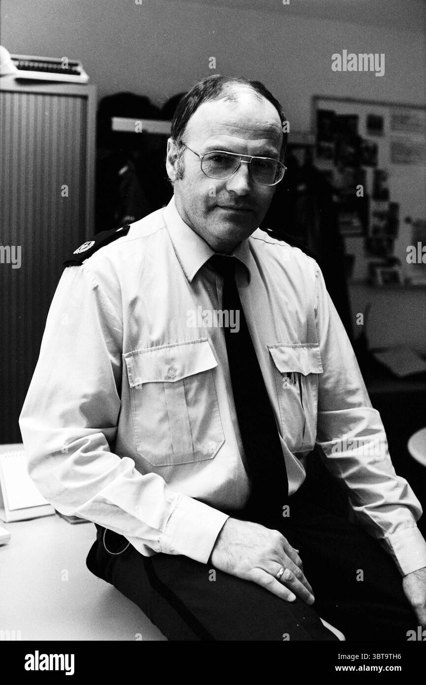 Polizei G. Muurling Porträt Haarlem Haarlem Niederlande, Whizgle News, Dutch Desk, Niederlande, 1950 - 2000 am 24-02-1997. Dies sind die Elemente im Bild. Die Szene zeigt eine Person mittleren Alters, die selbstbewusst auf einem Schreibtisch sitzt. Er hat kurze, sauber gekämmte Haare und trägt eine runde Brille, die seinen nachdenklichen Ausdruck unterstreicht. Die Kleidung besteht aus einem hellen Uniformhemd mit mehreren Taschen und einer dunklen Krawatte, die zu einem formellen, aber dennoch zugänglichen Aussehen beiträgt. Hinter ihm befindet sich ein Innenraum mit neutralen Wänden und gedämpfter Beleuchtung, die erzeugt Stockfoto