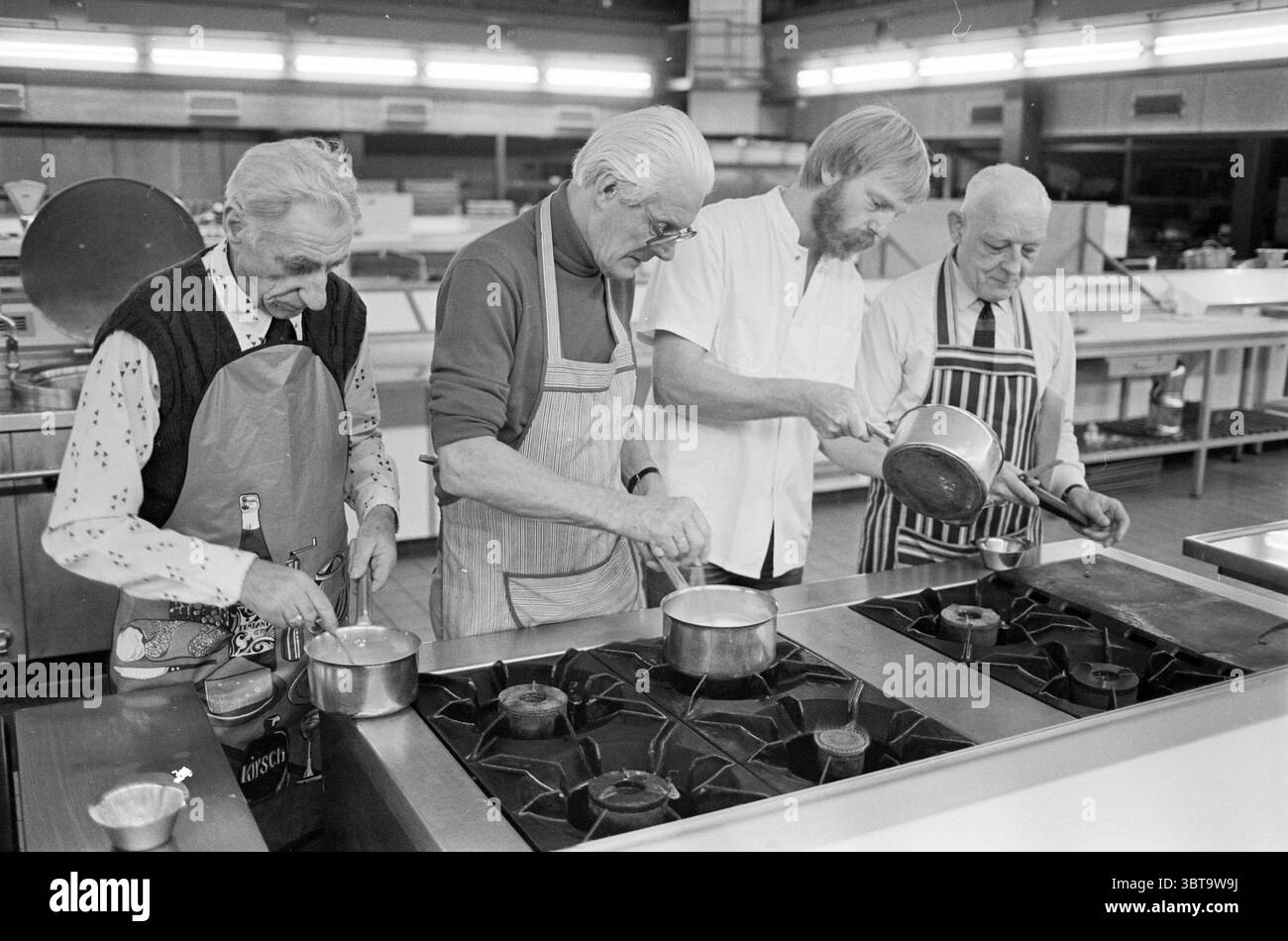 Kochkurs für Männer EC Cooking, Whizgle News, Dutch Desk, Niederlande, 1950 - 2000 am 22-11-1982. Das Bild enthält diese Themen. In einer belebten Küche stehen vier ältere Männer nebeneinander an einer Reihe von Gasherden, die sich jeweils auf ihre jeweiligen Töpfe konzentrieren. Das Ambiente strahlt ein Gefühl von Kameradschaft und Zweck aus. Die Küche ist gut beleuchtet, mit hellen Deckenleuchten, die die Szene beleuchten und die glänzenden Oberflächen und das metallische Kochgeschirr hervorheben. Die Männer sind in verschiedenen Schürzen gekleidet, was eine Mischung aus persönlichen Stilen andeutet. Einer trägt ein farbenfrohes, gemustertes Hemd unter einer einfarbigen Schürze Stockfoto