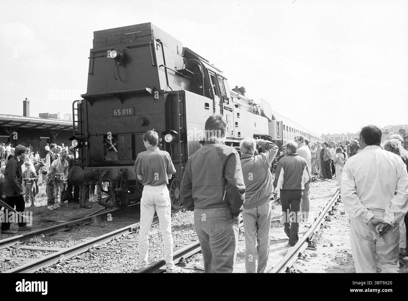 Ankunft der Dampfeisenbahn in IJmuiden. Trains IJmuiden the Netherlands, Whizgle News, Dutch Desk, Niederlande, 1950 - 2000 am 14-08-1987. Die Abbildung zeigt diese Themen. Auf einem belebten Bahnhofsgelände steht eine große Lokomotive, die sich durch ihre robuste und industrielle Bauweise auszeichnet, vorbildlich auf den Gleisen. Das Äußere ist ein tiefes, mattes Schwarz, das sich von den sanfteren Tönen der Umgebung abhebt. Die großen Räder und Motoren der Lokomotive deuten auf ihre kraftvollen Fähigkeiten hin, während die Anwesenheit mehrerer Abteile auf ein funktionales Design für Transport und Service hindeutet. Surr Stockfoto