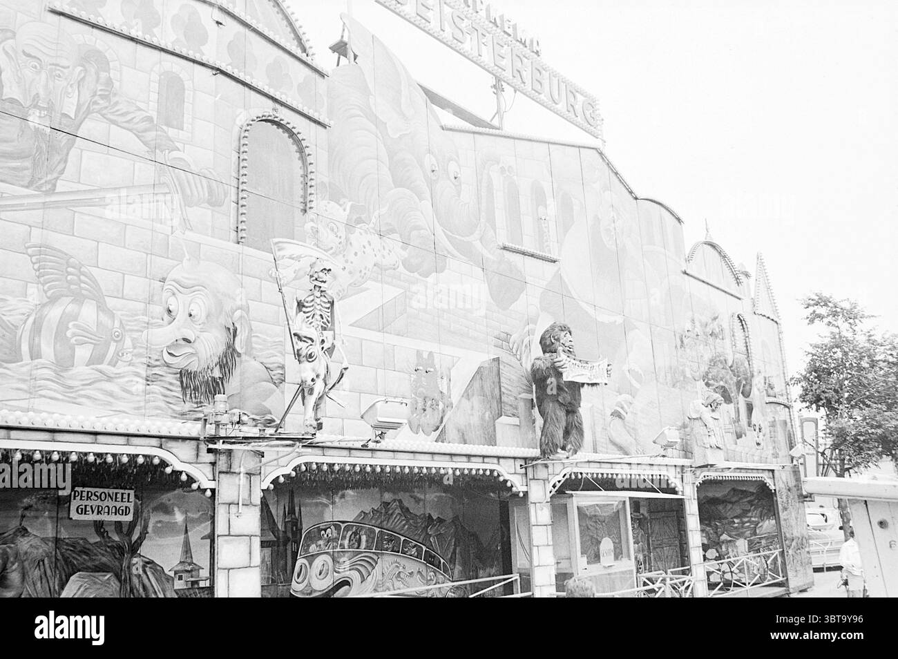 Fair Santpoort Santpoort, Whizgle News, Dutch Desk, Niederlande, 1950 - 2000 am 05-08-1969. Das Bild enthält diese Themen. Die Szene zeigt eine markante Fassade eines Vergnügungsbetriebs, die von komplizierten Wandgemälden gekennzeichnet ist, die die Außenwände bedecken. Diese Wandbilder zeigen skurrile und etwas fantastische Szenen, bevölkert von lebhaften Charakteren wie Tieren und mythischen Figuren, die eine verspielte und fröhliche Atmosphäre vermitteln. Die Farbpalette neigt sich stark in Schwarzweiß, sodass die Grafiken in Grautönen wiedergegeben werden. Das Fehlen lebendiger Farben verleiht eine nostalgische Qualität und erweckt einen Sinn o Stockfoto