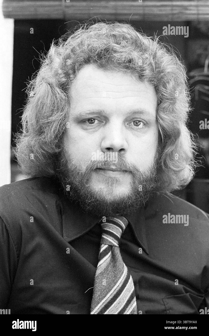 Porträt von Mr. Rusman kleine Beurs Football People and Trainer, Whizgle News, Dutch Desk, Niederlande, 1950 - 2000 am 05-04-1978. Diese Themen werden in der Abbildung angezeigt. Die Szene zeigt einen Mann mit einem ausgeprägten Erscheinungsbild, das von einer voluminösen, lockigen Frisur und einem vollen Bart geprägt ist. Sein Ausdruck ist ernst und vermittelt ein Gefühl der Besinnung oder der Introspektion. Er trägt ein dunkles Hemd mit Kragen, das im Kontrast zu den helleren Farben im Hintergrund steht und einen scharfen Blickpunkt auf seinem Gesicht schafft. Zusätzlich zu seinem formellen Erscheinungsbild trägt er eine Krawatte mit Streifenmuster, die Schatten enthält Stockfoto