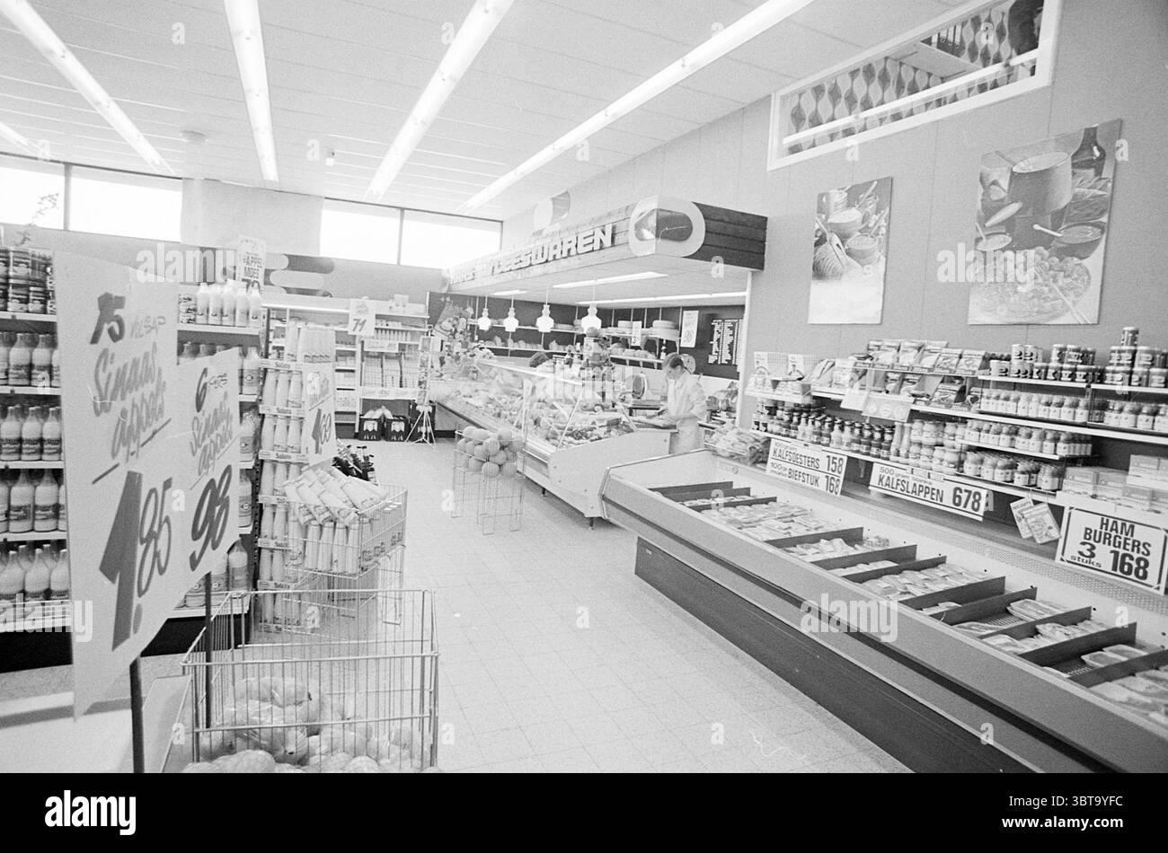 Intr. Beentjes -HeemskerkZuidervaart-Heemskerk Spar Super-Uitgeest. Innenausstattung, Whizgle News, Dutch Desk, Niederlande, 1950 - 2000 am 01-05-1974. Die Abbildung zeigt diese Themen. In einem geräumigen Lebensmittelgeschäft ist die Inneneinrichtung hell und sauber mit einer Dominanz von weiß- und Pastellfarben. Lange Leuchtstofflampen beleuchten den Raum von oben und schaffen eine gut beleuchtete Atmosphäre. Das Layout ist organisiert, die Gänge sind von Regalen gesäumt, die mit einer Vielzahl von Produkten, darunter Dosenwaren und verschiedene verpackte Artikel, bestückt sind. Links befindet sich ein Abschnitt mit frischen Produkten, in dem ein VAR steht Stockfoto