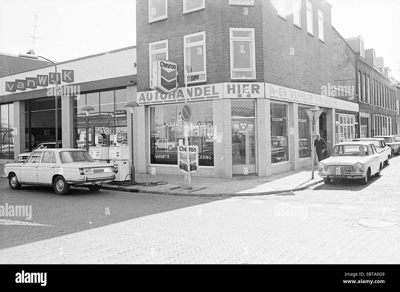 Erw. Jugendzentrum d'Appelaer extern. Jugendzentrum Kampersingel ext. Garage Amsterdamsevaart Exterior Haarlem Kampersingel Niederlande, Whizgle News, Dutch Desk, Niederlande, 1950 - 2000 am 22-03-1972. Diese Themen werden in der Abbildung angezeigt. Die Szene zeigt eine charmante Straßenecke in Schwarz-weiß-Ästhetik, die eine nostalgische Atmosphäre weckt. Auf der linken Seite befindet sich eine gut gepflegte Tankstelle mit einem schlanken, modernen Design mit großen Fenstern und einem markanten Schild, das die Marke unterstreicht. Die leicht abgenutzten und dennoch funktionalen Gaspumpen deuten auf ein hektisches Leben hin. Direkt auf der anderen Straßenseite befindet sich ein Auto Stockfoto