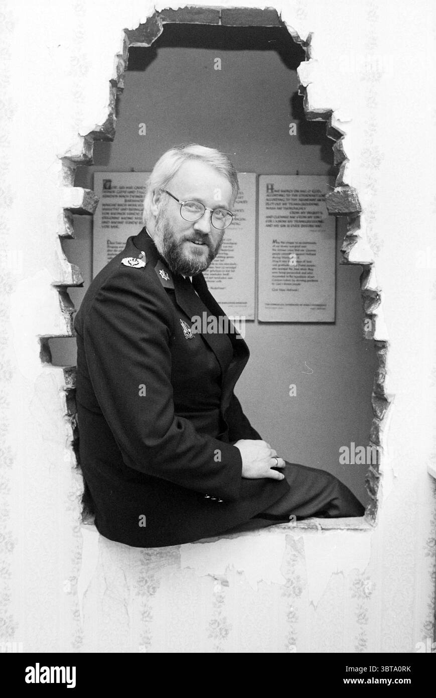 Eine Präsentation eines Buches im Corrie Ten Boomhuis Museum Haarlem Barteljorisstraat 19 the Netherlands, Whizgle News, Dutch Desk, Niederlande, 1950 - 2000 am 09-03-1994. Diese Themen sind in der Abbildung dargestellt. In dieser Szene sitzt ein Mann bequem in einer großen, unregelmäßig geformten Öffnung in einer scheinbar wie eine Wand. Die Umgebung ist durch hübsche Tapeten mit einem hellen Blumenmuster gekennzeichnet, die sich von den rauen, zerklüfteten Kanten des Lochs abheben. Die Kleidung des Mannes trägt eine dunkle Uniform mit verschiedenen Insignien, die Autorität und Professionalität vermitteln. Sein Bart und seine Brille geben ihm Stockfoto