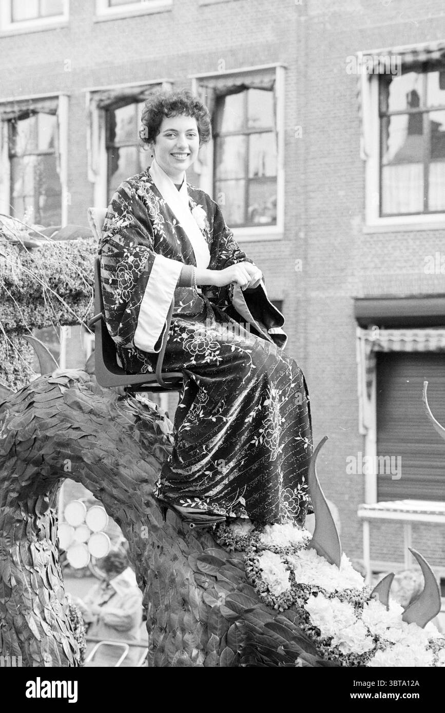 Tulip Queen auf KLM Parade Float Flower Parade Blumenausstellung, Whizgle News, Dutch Desk, Niederlande, 1950 - 2000 am 22-04-1988. Das Bild enthält diese Themen. In einer lebhaften Feier sitzt eine junge Frau auf einem großen Wagen und verkörpert einen Hauch von Eleganz. Sie trägt ein fließendes Kleid, das mit komplizierten Mustern verziert ist und einen reichen Kontrast zu den gedämpften Tönen ihrer Umgebung zeigt. Der Stoff blitzt und fängt das Licht auf eine Weise ein, die seine Schönheit unterstreicht. Der Schwimmer selbst ist mit einer Vielzahl von bunten Blumen dekoriert, die sich durch das Design mit organischen Kurven winden und die Verschönerung verstärken Stockfoto