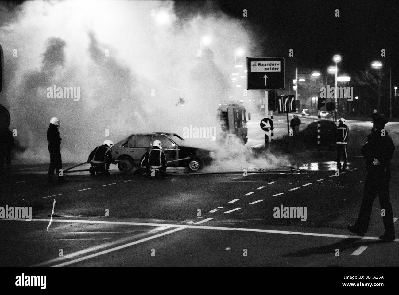 Old + New Haarlem Haarlem Oudeweg the Netherlands, Whizgle News, Dutch Desk, Niederlande, 1950 - 2000 auf 31-12-1990. Diese Themen sind in der Abbildung dargestellt. Die Szene entfaltet sich in einer nächtlichen Umgebung, die von einer dichten Rauchwolke gekennzeichnet ist, die sich nach oben bläht und die Sicht teilweise verdunkelt. Die Atmosphäre ist angespannt und chaotisch, mit einem starken Kontrast zwischen Hell und Dunkel. Beleuchtete Bereiche zeigen das Vorhandensein von Rettungsfahrzeugen, die ihre Lichter blinken – vielleicht rot und blau – und dynamische Farbtöne gegen die Schatten setzen. Im Vordergrund steht eine Gruppe von Individuen, die in dunklen Uniformen gekleidet sind, entschlossen. Die Stockfoto