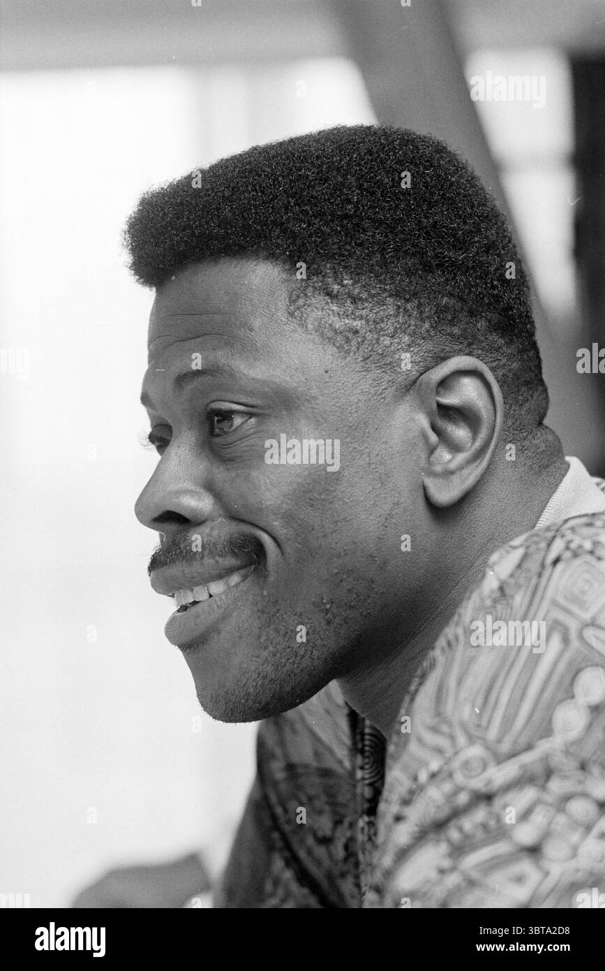 Patrick Ewing 'Dream Team', Whizgle News, Dutch Desk, Niederlande, 1950 - 2000 am 07.09.1992. Dies sind die Elemente im Bild. Die Szene zeigt einen Mann im Profil, der ein warmes und fesselndes Lächeln zeigt. Sein Haar ist in einem kurzen, voluminösen Schnitt gestylt, der die Konturen seines Gesichts hervorhebt. Er hat einen starken Kiefer und hervorstechende Merkmale, die ein Gefühl von Selbstvertrauen und Zugänglichkeit vermitteln. Er trägt ein gemustertes Kleidungsstück, das visuell interessant ist, mit komplizierten Designs, die auf kulturelle Bedeutung hinweisen. Die Farben im Material wirken kräftig und lebendig und tragen zu einer insgesamt warmen Wärme bei Stockfoto