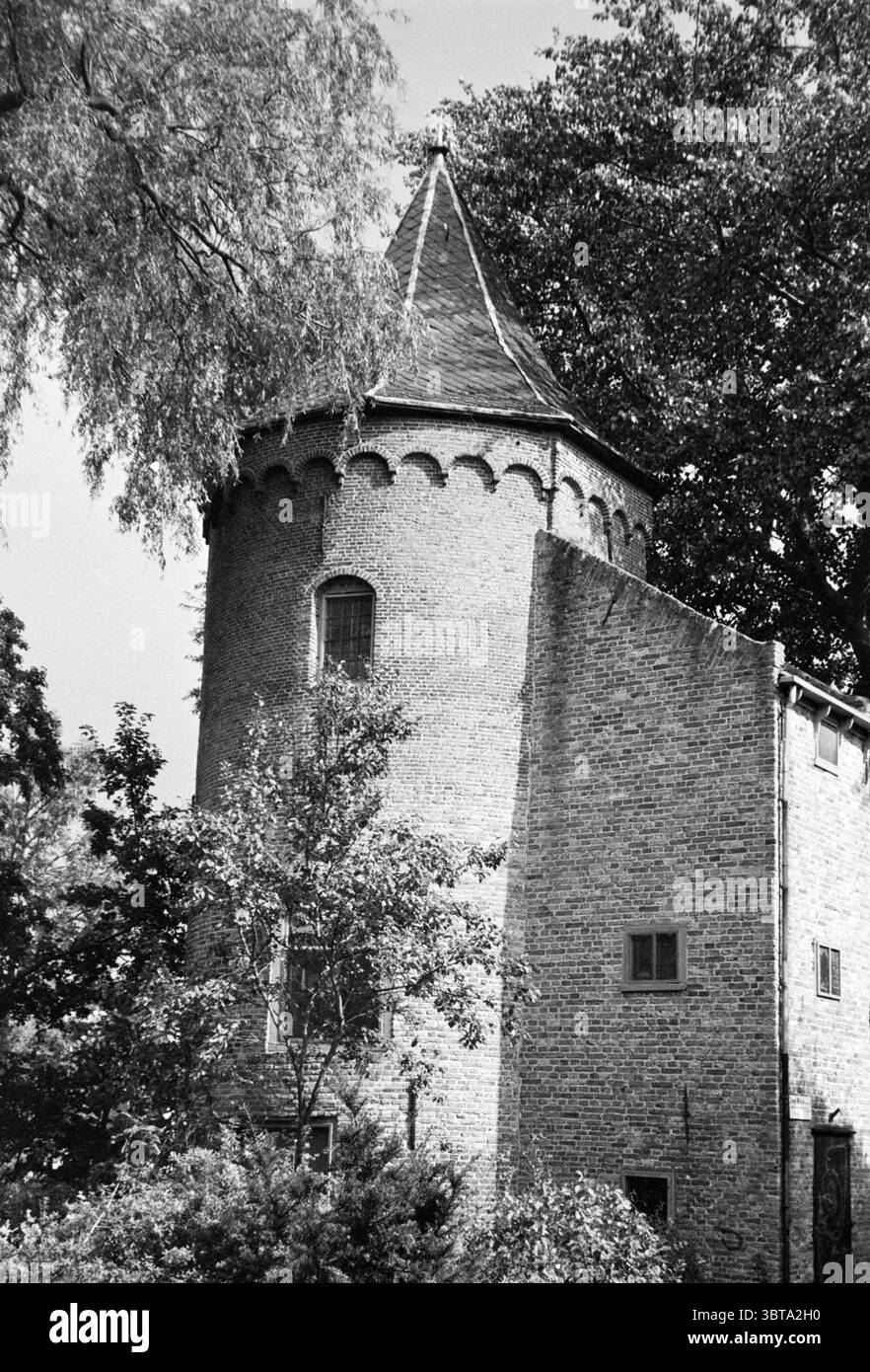 Castle, Whizgle News, Dutch Desk, Niederlande, 1950 - 2000 am 09-1985. Das Bild enthält diese Themen. Die Szene zeichnet sich durch eine malerische, turmförmige Struktur aus, die sich durch ihr einzigartiges architektonisches Design auszeichnet. Das Gebäude ist aus einem warmen Ziegelstein gefertigt und weist eine Erdpalette auf, die sich harmonisch in die Umgebung einfügt. Der Turm mit seinem konischen Dach fügt der Gesamtsilhouette ein skurriles Element hinzu, ergänzt durch eine Reihe von strukturierten Zinnen oben. Im Vordergrund umgibt ein reichhaltiges Laubwerk die Basis des Gebäudes. Verschiedene Farbtöne o Stockfoto