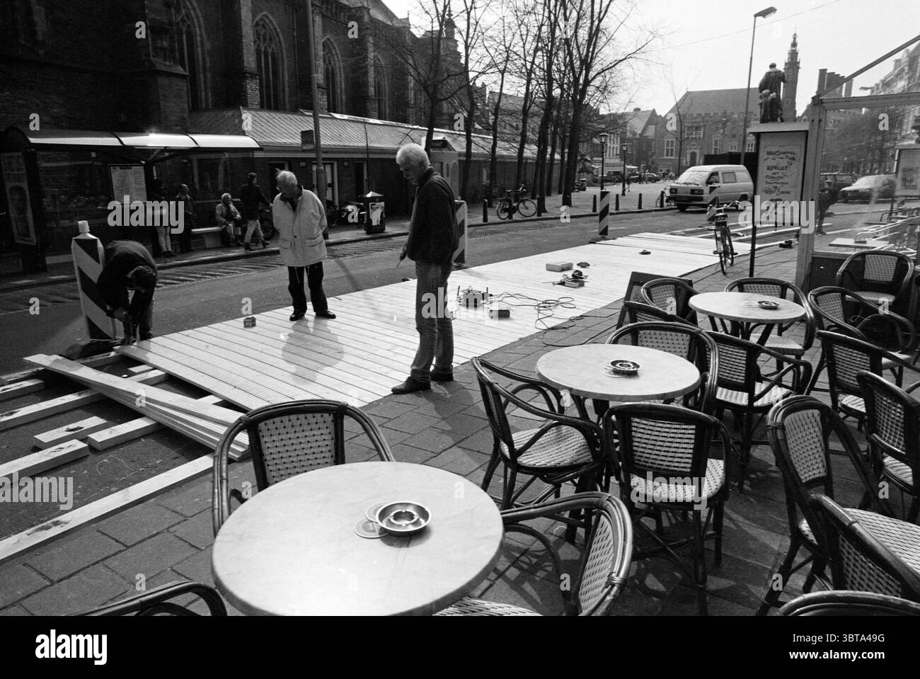 Neue Terrasse am Grote Markt Haarlem Grote Markt Niederlande, Whizgle News, Dutch Desk, Niederlande, 1950 - 2000 am 20-04-1994. Das Bild enthält diese Themen. Die Szene entfaltet sich in einer belebten Straßenecke, in der zwei Personen an einem Bau- oder Installationsprojekt auf einer neu verlegten Holzplattform, die sich über den Bürgersteig erstreckt, beteiligt sind. Eine Person, die in einem hellen Mantel gekleidet ist, liegt auf den Knien und konzentriert sich intensiv, während sie mit Werkzeugen arbeitet, während die andere in der Nähe steht und den Fortschritt beobachtet. Um sie herum ist eine lebhafte urbane Umgebung, wo eine Reihe Stockfoto