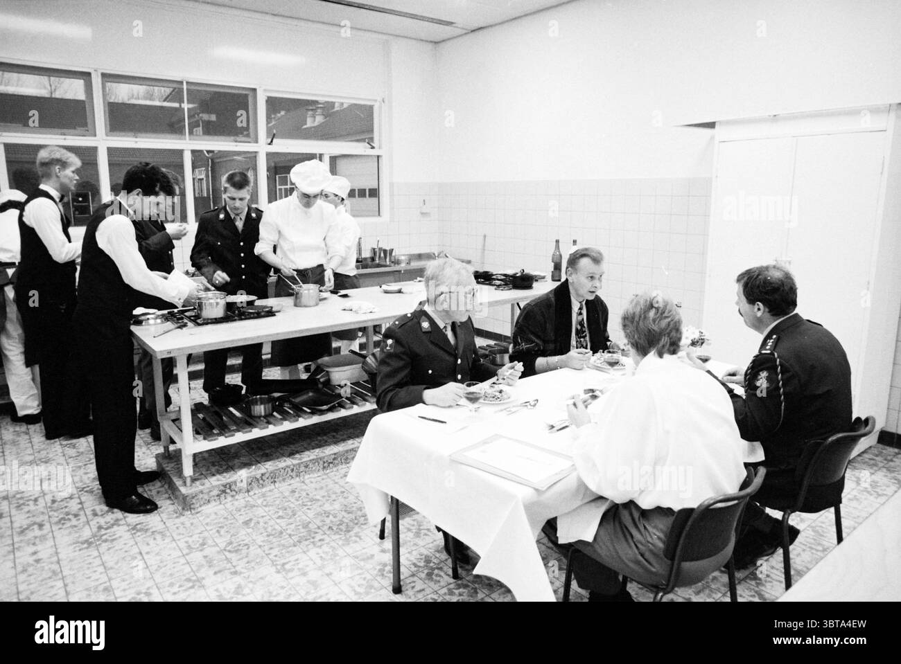 Ripperda Barracks Kochwettbewerb Haarlem the Netherlands, Whizgle News, Dutch Desk, Niederlande, 1950 - 2000 am 08-04-1991. Diese Themen sind in der Abbildung dargestellt. In einer geräumigen Küche, verschiedene Gruppen von Einzelpersonen in verschiedenen Bereichen. Auf der einen Seite sind mehrere Köche und Küchenmitarbeiter in dunklen Uniformen und Schürzen aktiv mit der Zubereitung von Speisen beschäftigt. Ihre Bewegungen deuten auf eine koordinierte Anstrengung hin, wenn sie Töpfe und Pfannen auf dem Herd handhaben. Ein Chefkoch mit einem hohen weißen Hut steht im Vordergrund und zeigt einen Schwerpunkt der Autorität in der geschäftigen Atmosphäre. Zur Opposi Stockfoto