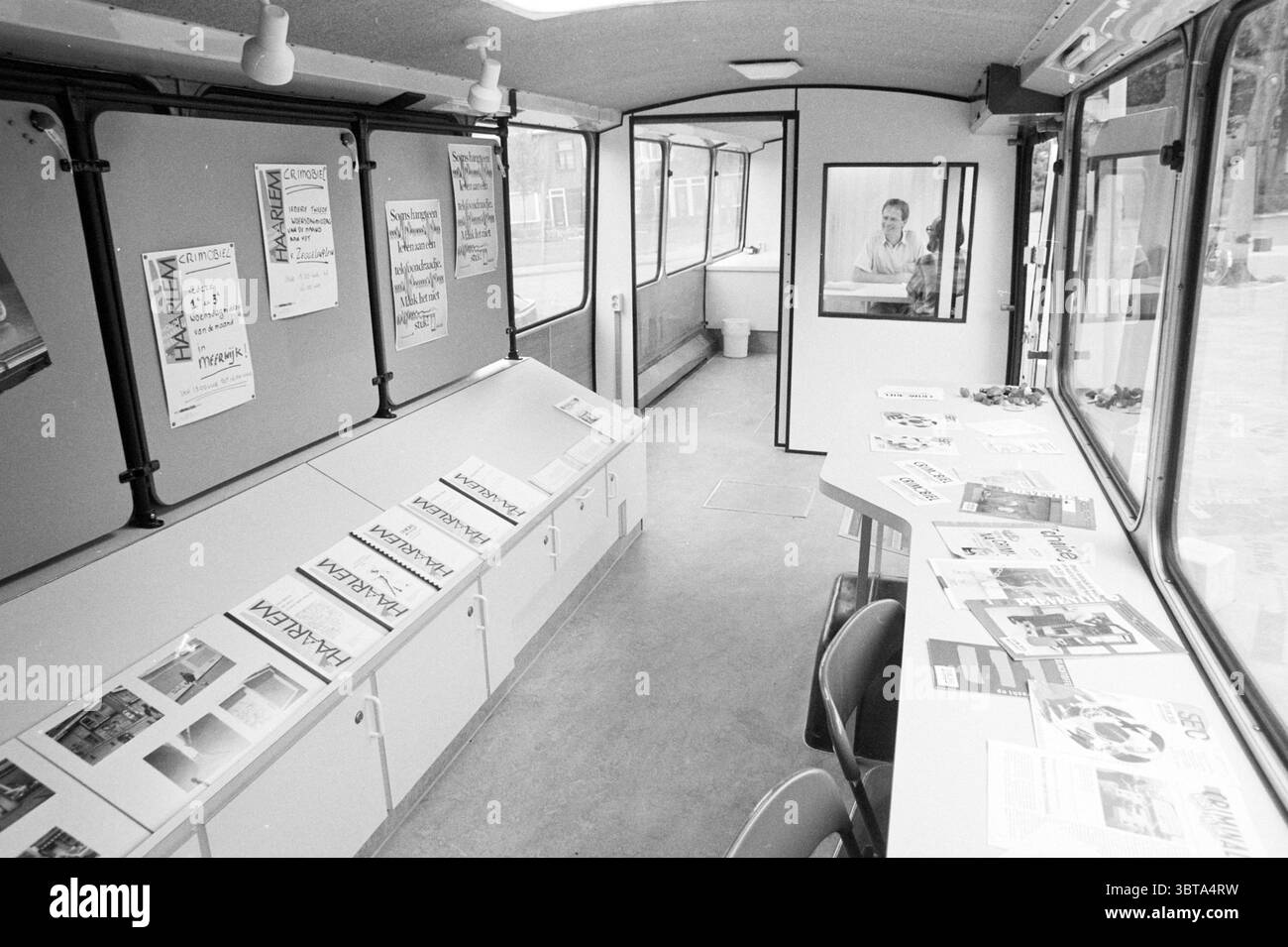 Crimobile Liveability Unsicherheit Vandalismus Haarlem the Netherlands, Whizgle News, Dutch Desk, Niederlande, 1950 - 2000 am 09-1990. Dies sind die Elemente im Bild. Die Szene verfügt über ein geräumiges, modernes Interieur, das einem mobilen Ausstellungs- oder Informationsraum ähnelt. Die vorherrschenden Farben sind gedämpft, mit Grautönen und Anklängen von weiß, was zu einer minimalistischen und sauberen Ästhetik beiträgt. Auf einer Seite des Raumes befindet sich eine lange Arbeitsplatte mit glatter Oberfläche, die eine Sammlung von Materialien, die ordentlich angeordnet sind, möglicherweise Broschüren oder Informationsblätter. Die Arbeitsplatte wird ergänzt Stockfoto
