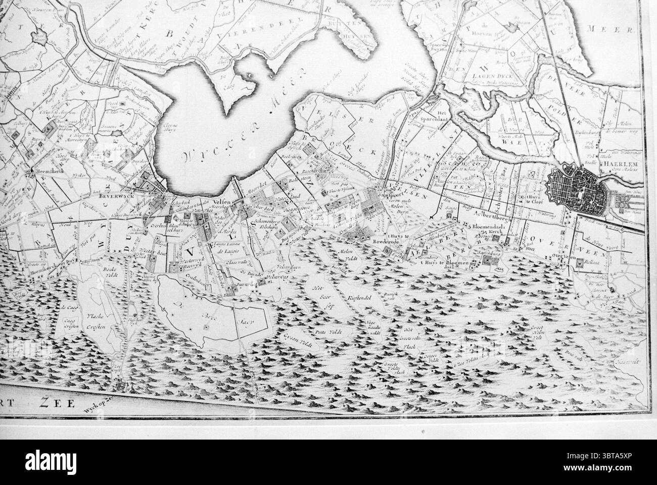 Karte von IJmuiden um 1720 IJmuiden Niederlande, Whizgle News, Dutch Desk, Niederlande, 1950 - 2000 am 07-07-1994. Dies sind die Elemente im Bild. Die Szene zeigt eine detaillierte und komplizierte Darstellung eines geografischen Gebiets, das durch eine Vintage-monochrome Ästhetik gekennzeichnet ist. Im Vordergrund deuten eine Reihe von Wellenlinien auf das Vorhandensein von Wasser hin, möglicherweise auf einen See oder Fluss, wobei sanfte Wellen ein Gefühl von Bewegung erzeugen. Um dieses Gewässer herum symbolisieren eine Vielzahl kleiner, akribisch gezeichneter Formen das Land, die möglicherweise Inseln oder nahe gelegene Küsten darstellen. Diese Stockfoto