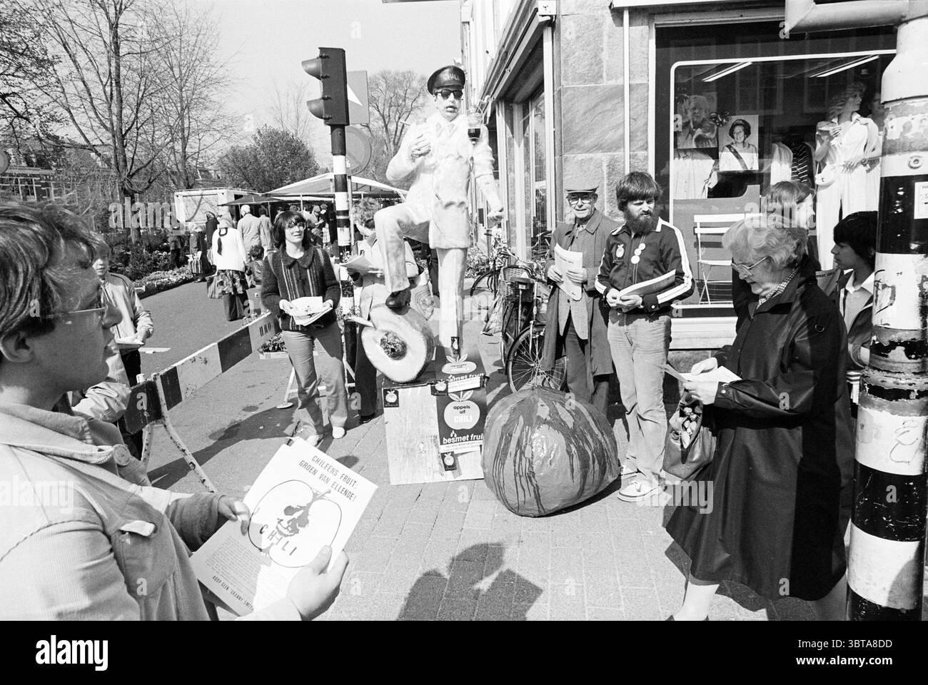 Chile Demonstration Grote Houtstraat Demonstration Haarlem Grote Houtstraat Niederlande, Whizgle News, Dutch Desk, Niederlande, 1950 - 2000 am 02-05-1980. Dies sind die Elemente im Bild. Die Szene zeigt eine lebhafte Stadtstraße mit vielen Menschen und Aktivitäten. Im Vordergrund steht ein junger Mensch mit einem Flyer in der Hand und führt Gespräche mit einer Gruppe in der Nähe. Sie tragen ein lässiges Outfit, und ihr Ausdruck deutet auf Neugier oder Begeisterung hin. Auf der linken Seite steht ein Statue-ähnlicher Darsteller, der in einem hellen Anzug gekleidet ist, auf einem Podest und hält einen Drink. Diese Person ist der foca Stockfoto
