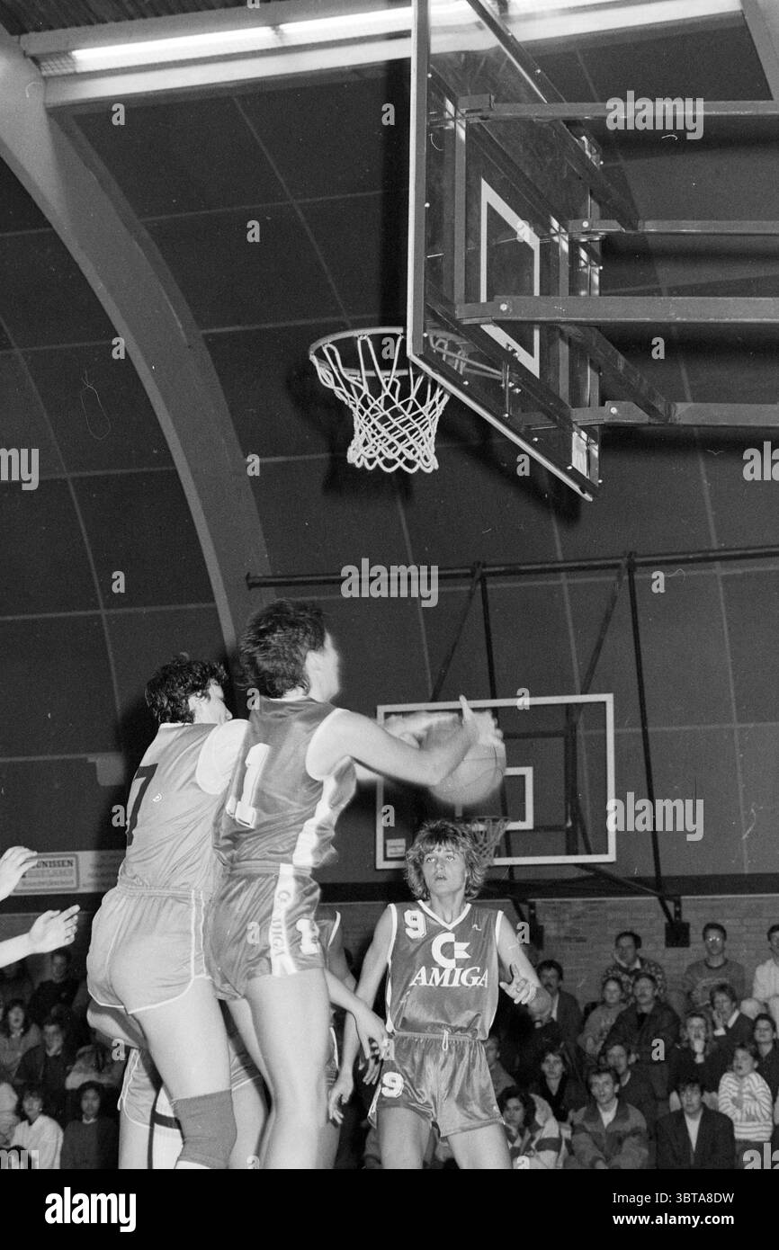 Basketball. Wettbewerb Amiga- ?, Whizgle News, Dutch Desk, Niederlande, 1950 - 2000 auf 30-12-1989. Dies sind die Elemente im Bild. Die Szene entfaltet sich in einem dynamischen Basketballfeld, wo die Energie spürbar ist. Zwei Spieler, die in unterschiedliche Uniformen gekleidet sind, befinden sich in einem angespannten Moment des Spiels. Ein Athlet, der ein Trikot trägt, das mit einer auffälligen Zahl „1“ markiert ist, bereitet sich auf einen Schuss vor. Die Muskeln sind angespannt und konzentriert. Der andere Spieler, der mit der Zahl „7“ markiert ist, scheint gegen das Spiel anzutreten und streckt einen Arm, um den Schuss zu blockieren. Der Spieler, der den Korb versucht, ist positioniert Stockfoto